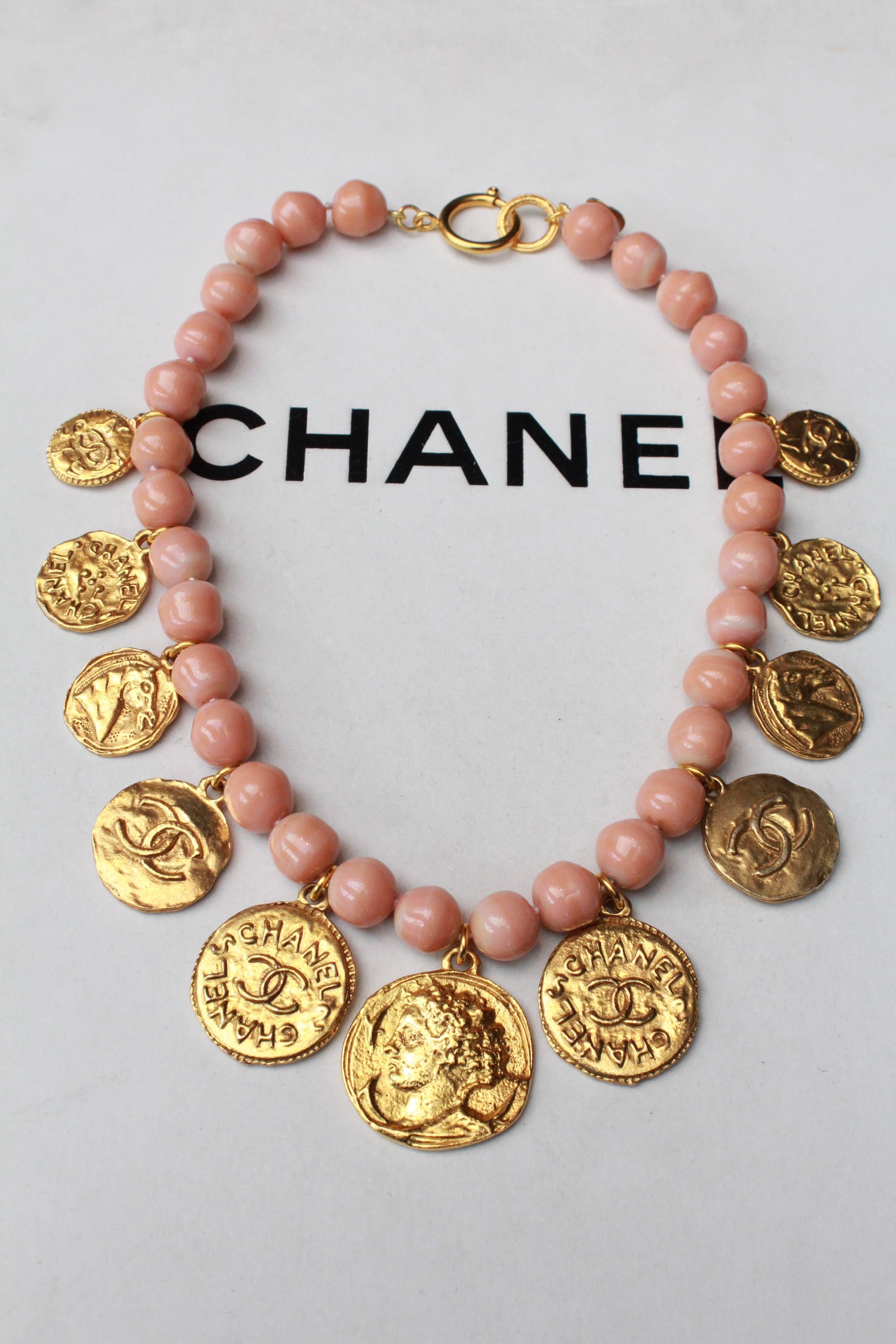 CHANEL (Made in France) Choker made of powder pink beads decorated all along with small stamped gilded metal medals representing coins.  Each medallion features a different motif, such as the brand logo, Gabrielle Chanel’s portrait or