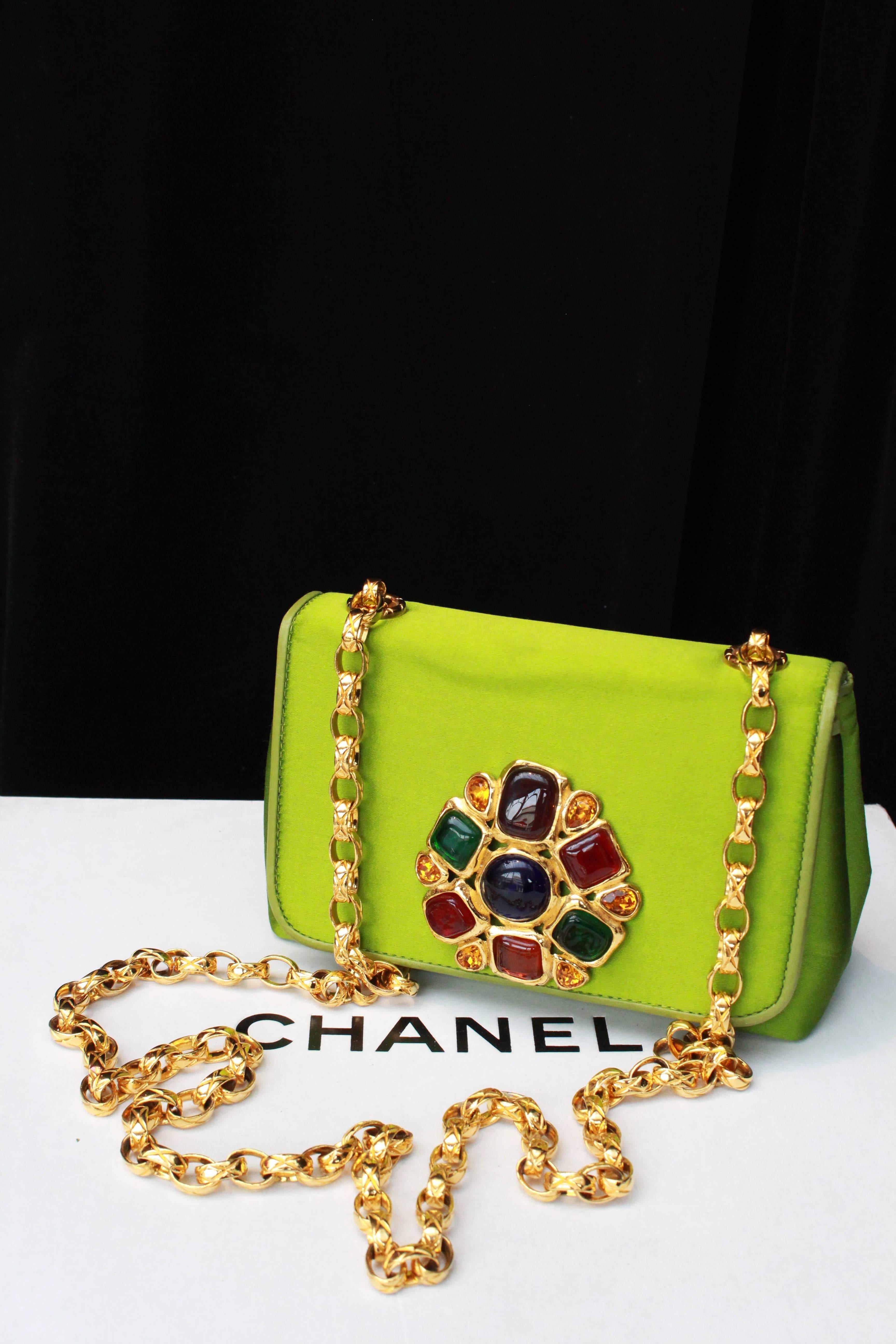 CHANEL (Made in Italy)  – Green satin jewel evening shoulder bag. The flap is embellished with a gilded metal jewel paved with ruby, emerald, sapphire and amber glass paste cabochons. The long gilded metal shoulder strap is made of quilted links.
