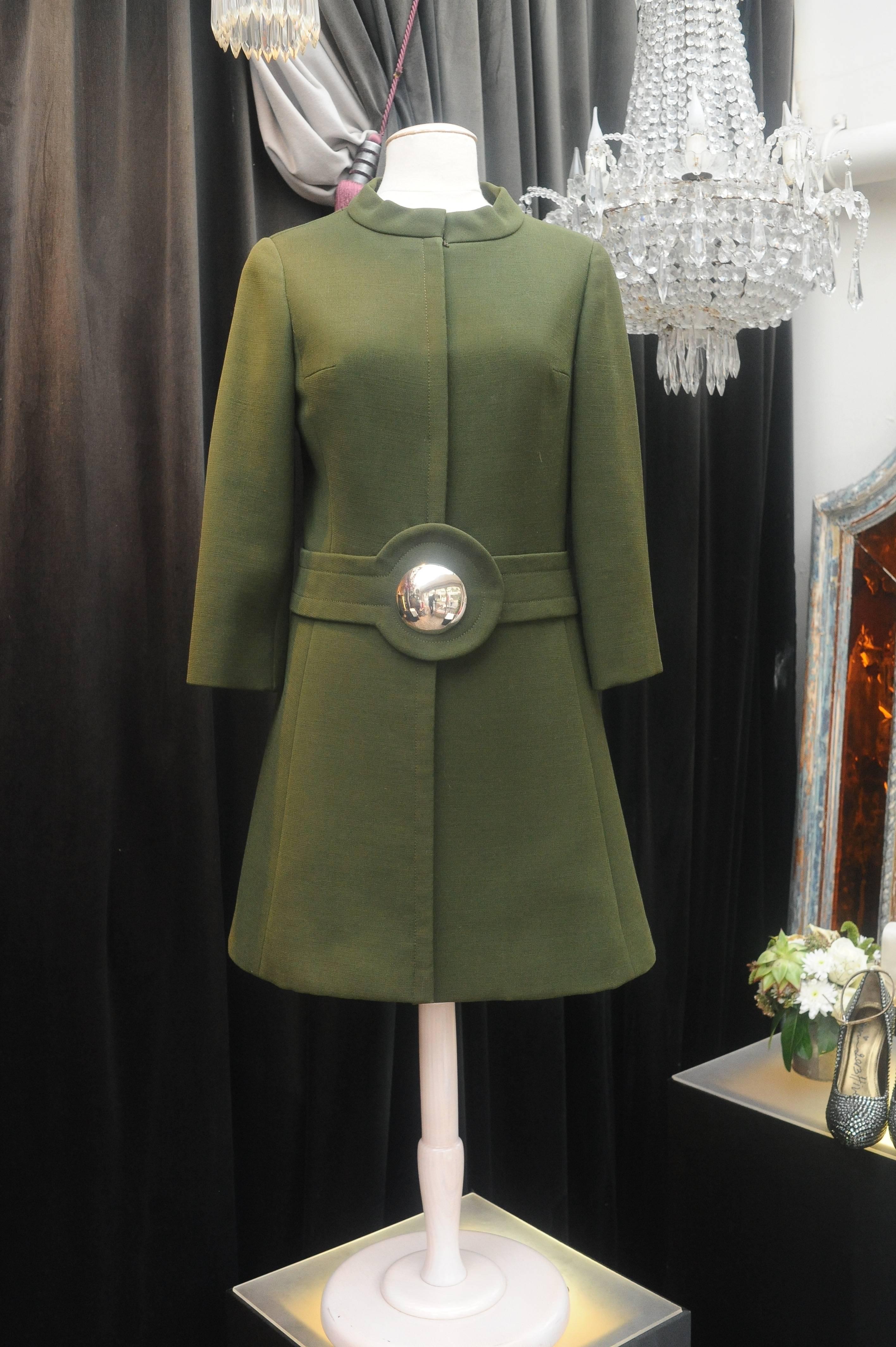 Pierre Cardin Boutique Paris – Short coat composed of khaki green wool, with snaps closure. The waist is emphasized with a fake belt featuring a concave silvery half sphere. Brown lining.

Circa 1960.

No indicated size, fits a 36/38 (US 4/6