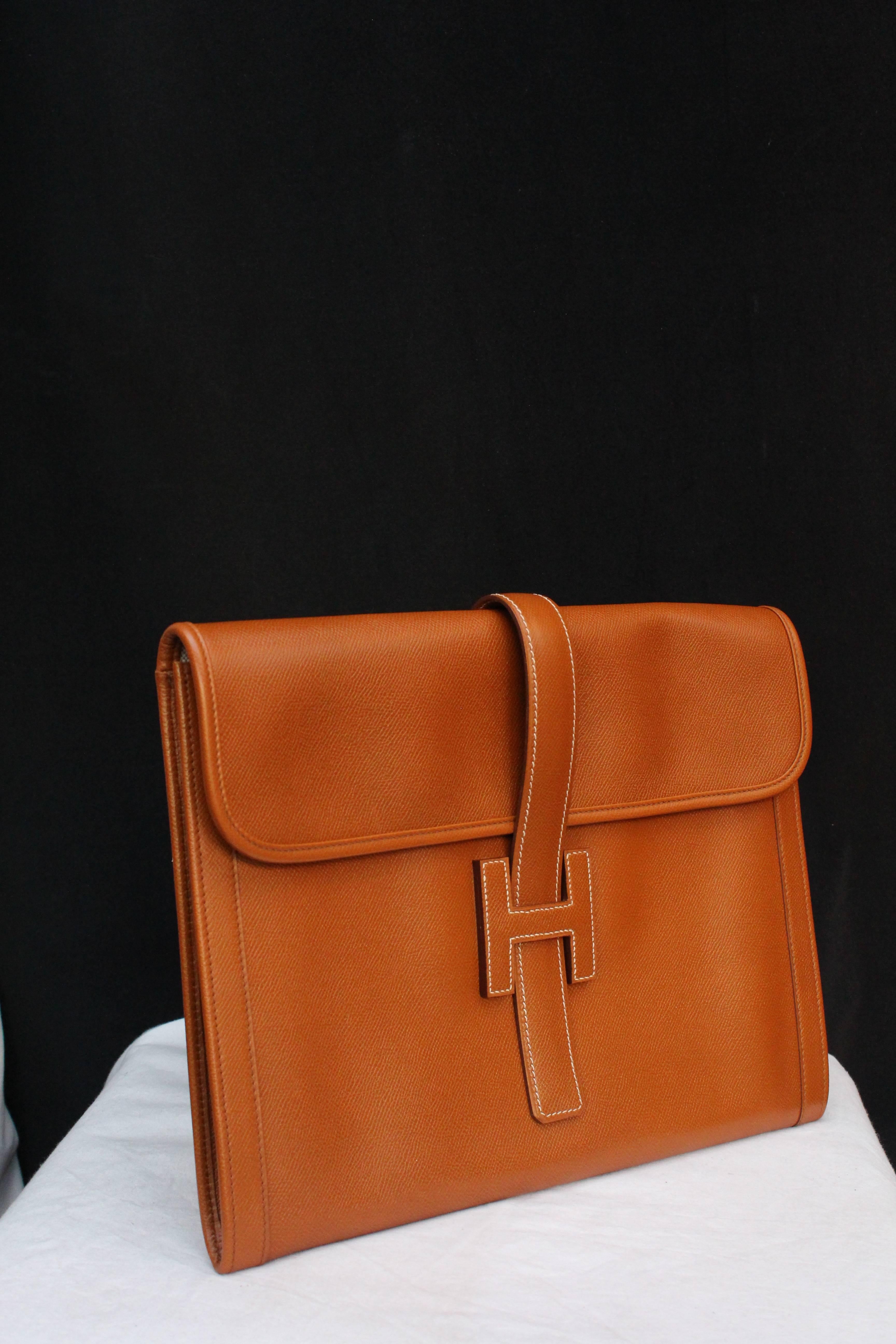 HERMES (Made in France) “Jige” clutch in tan color togo leather. It opens with a leather strap going through the H clutch. Beige fabric lining.

Width 34 cm (13.5 in); height 25 cm (10 in); Depth 2 cm (0.75 in).

Very good condition, apart from a