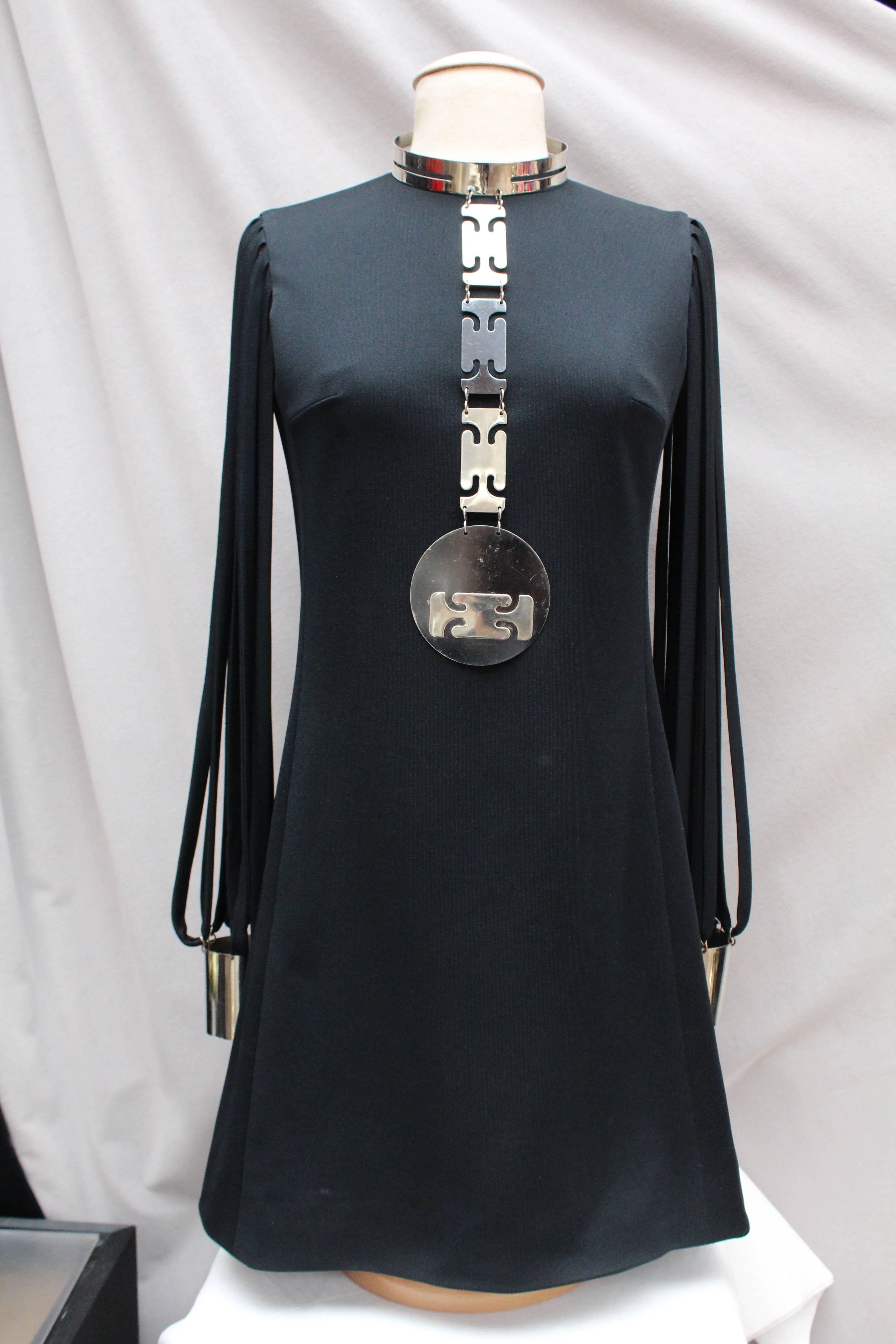 PIERRE CARDIN (Attributed to – Made in France) Little black jersey dress with trapezoid cut, round collar and “couture” long sleeves. The sleeves are composed of thin straps revealing the arms from shoulder to cuffs. The straps are linked together