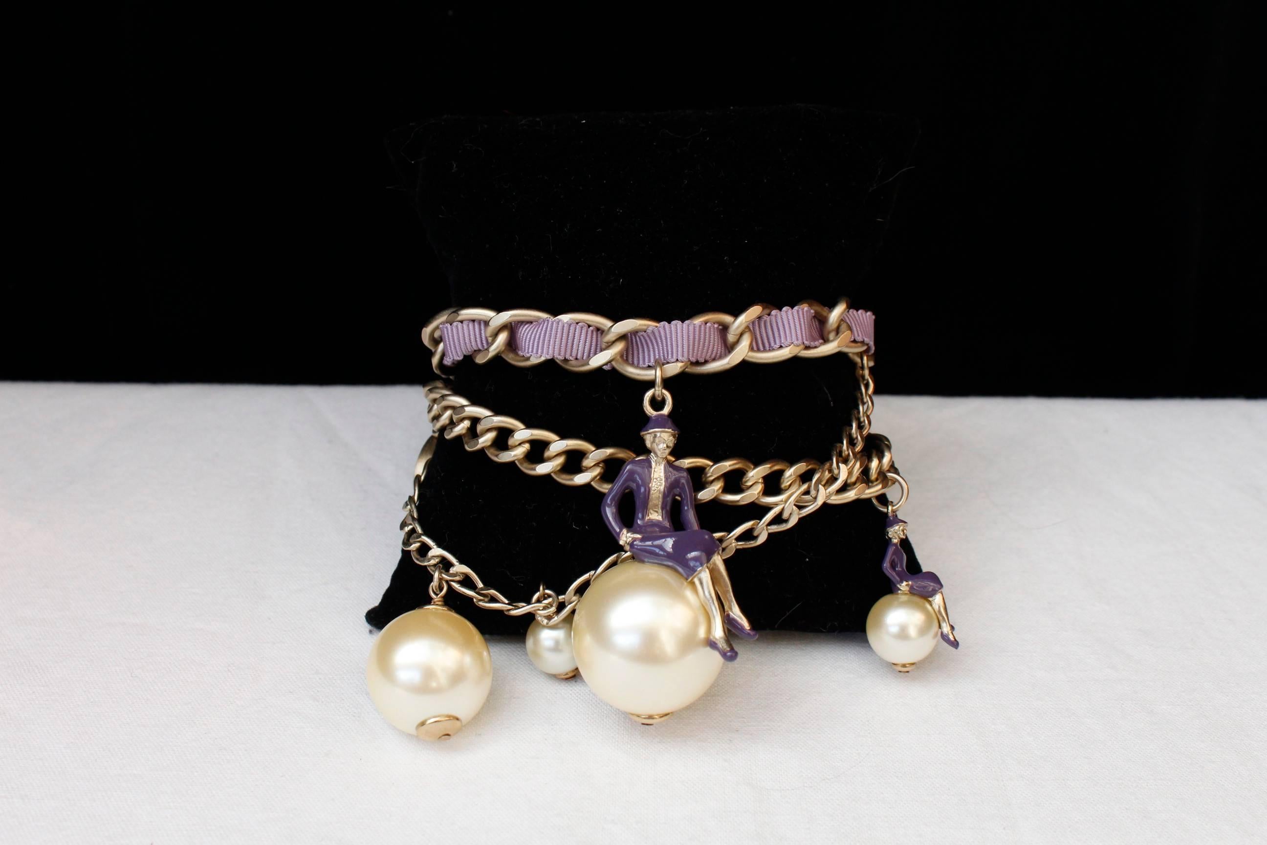 CHANEL (Made in France) Bracelet composed of three strands of curb chain in light gold gilded metal, embellished with purple tweed, faux-pearls, small CC logos in enamelled purple color and two figurines representing Coco Chanel sitting on a bead.