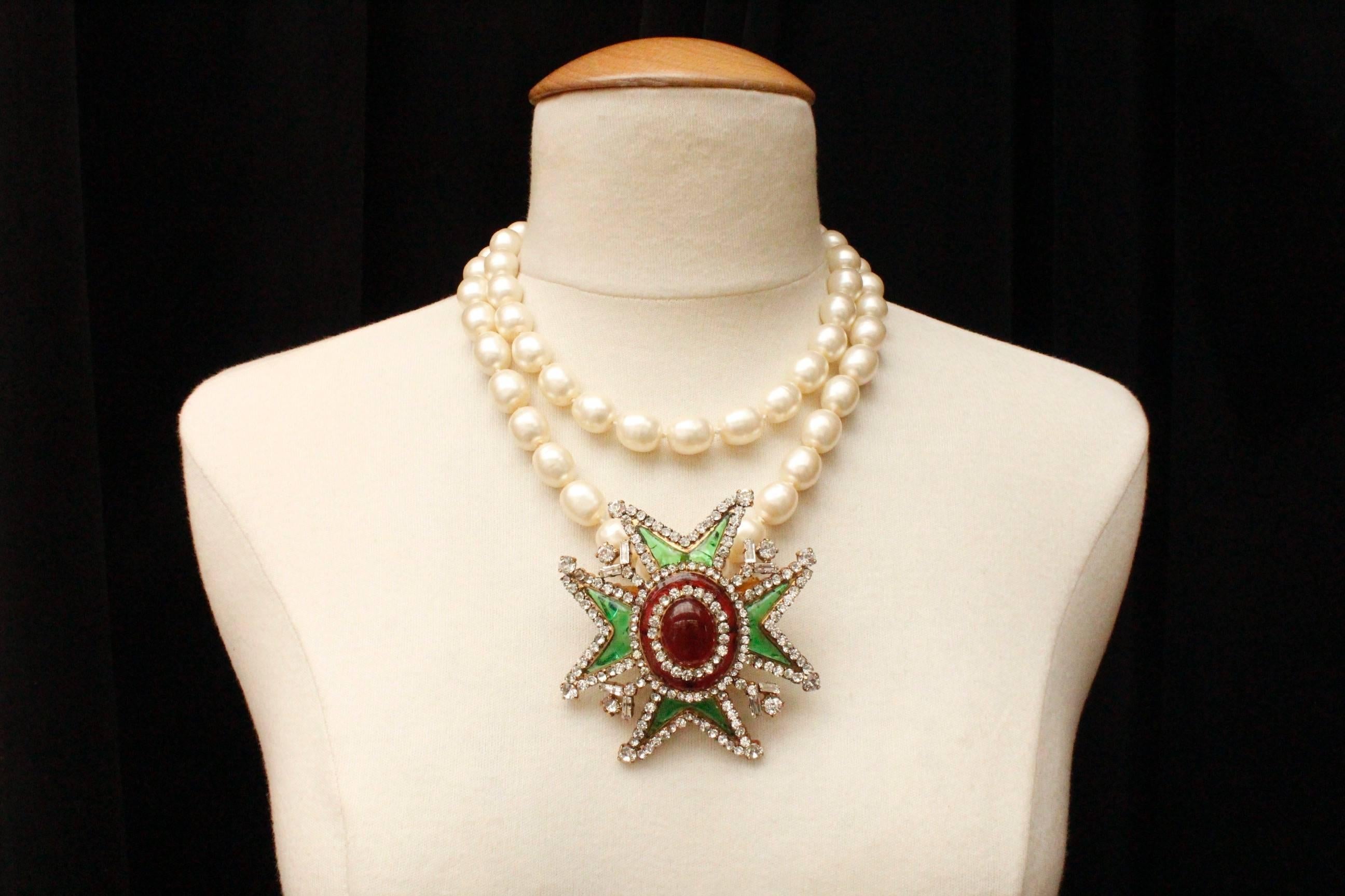 CHANEL (Made in France) Long necklace composed of knot mounted baroque faux-pearl  and a pendant representing a Maltese cross. The gilded metal pendant is paved with Swarovski crystals and ruby and emerald poured glass paste. The pendant can be worn