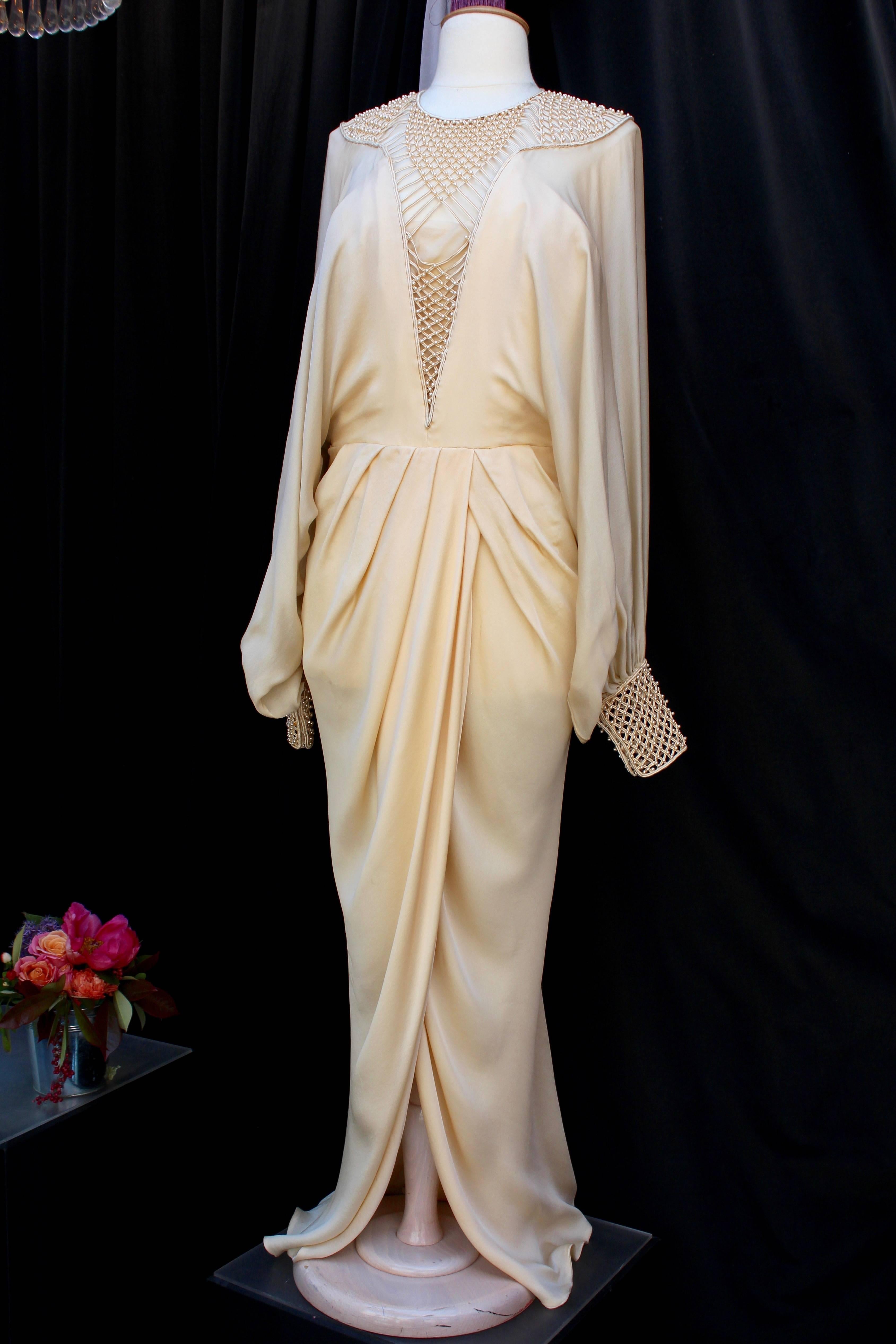 LOUIS FERAUD Haute Couture (Made in France) beautiful evening gown made of ivory silk. A wide openwork passementerie breastplate, held by a tonal corset, embellished with pearly beads, underlines the neckline. The batwing sleeves  are tightened with
