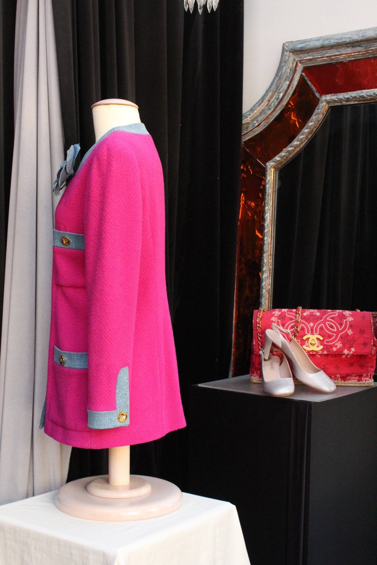 Chanel Boutique jacket (Made in France) from the 1990s, composed of bright and happy pink woolen fabric adorned with strips of denim and a camellia flower brooch in denim. 

The jacket with a V-neck closes thanks to gold metal buttons at the front