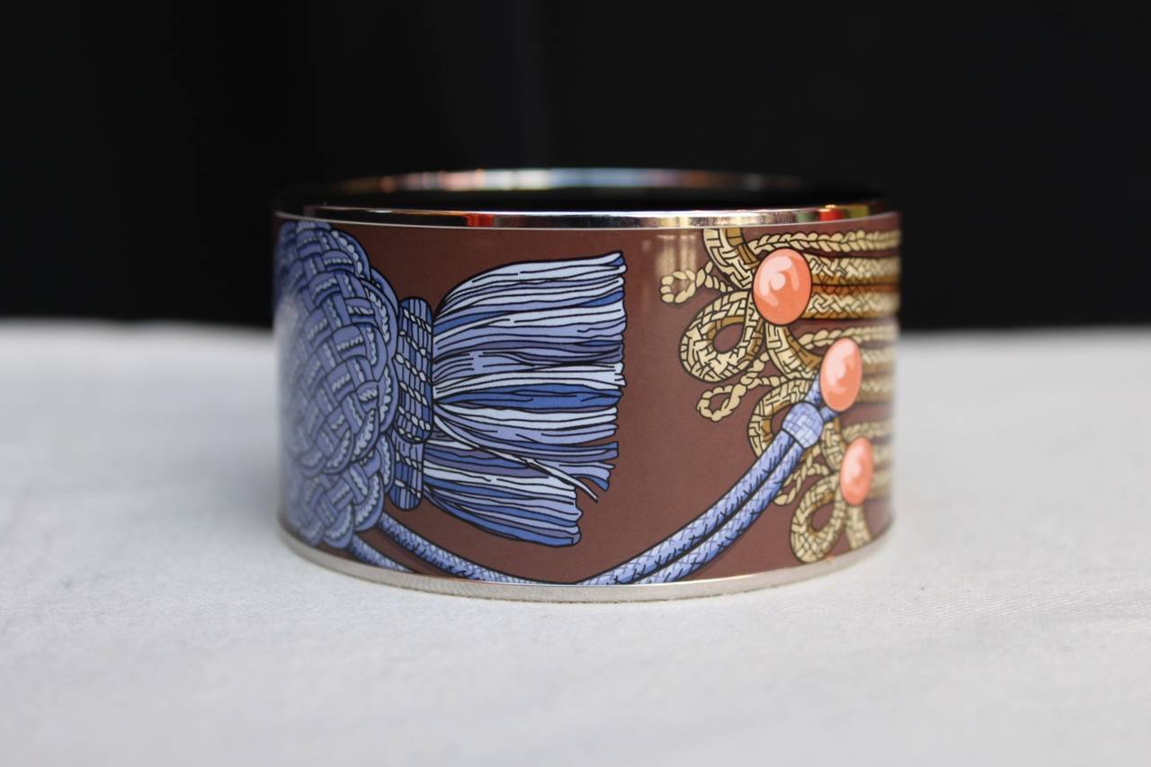 Large Hermes bangle (Made in France) composed of silver metal lining and cloisonné enamel featuring a trimming design in chocolate, blue, beige and pink. 

In the internal face of the bangle is displayed an embossed internal gold logo and a O