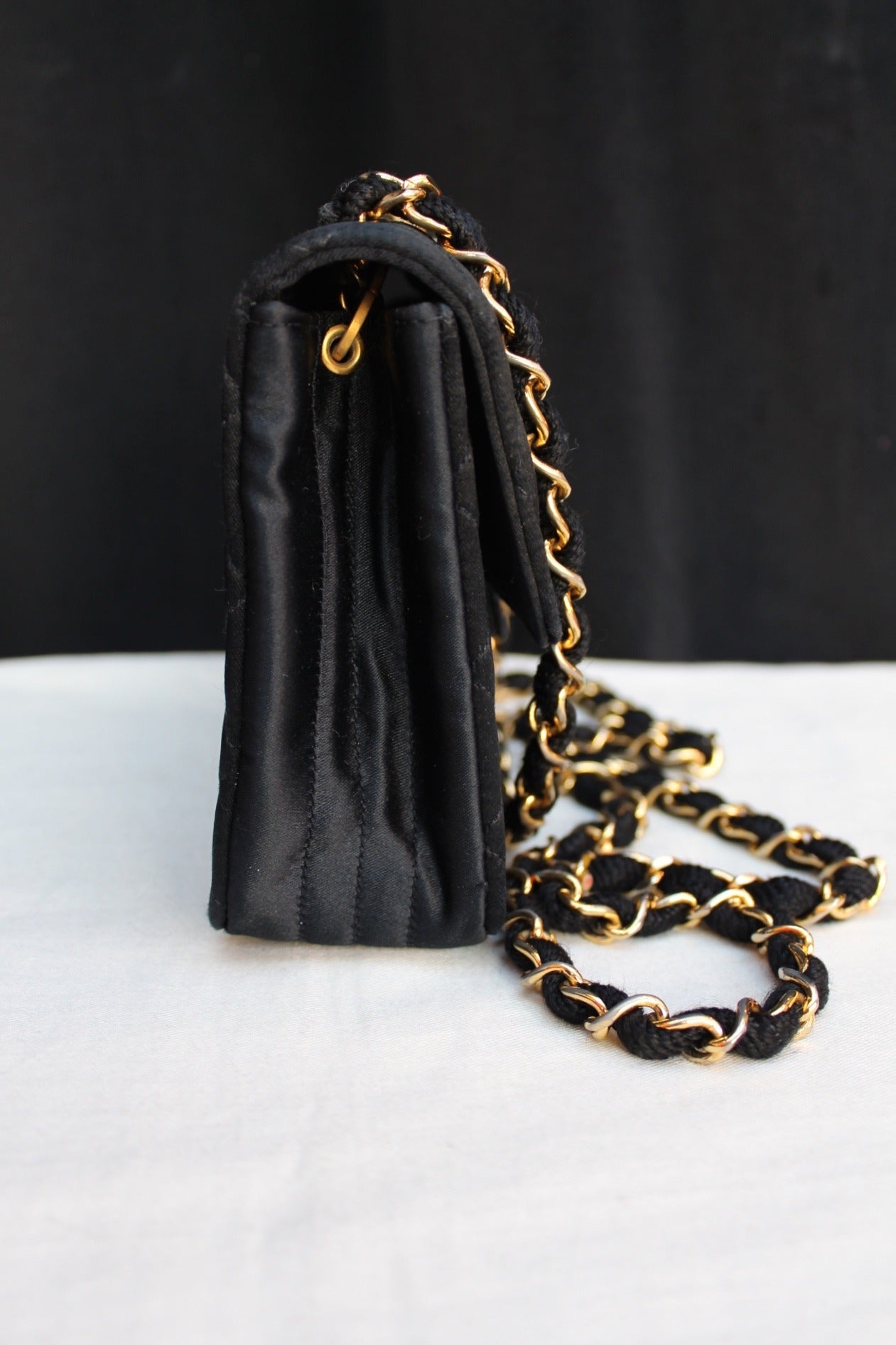 Very chic Chanel bag in black quilted satin adorned with a gold metal chain interlaced with black rope, and front flap with large gold plated CC twist lock. 

The bag can be worn as a cross body bag. 

The bag contains two patch pockets and one