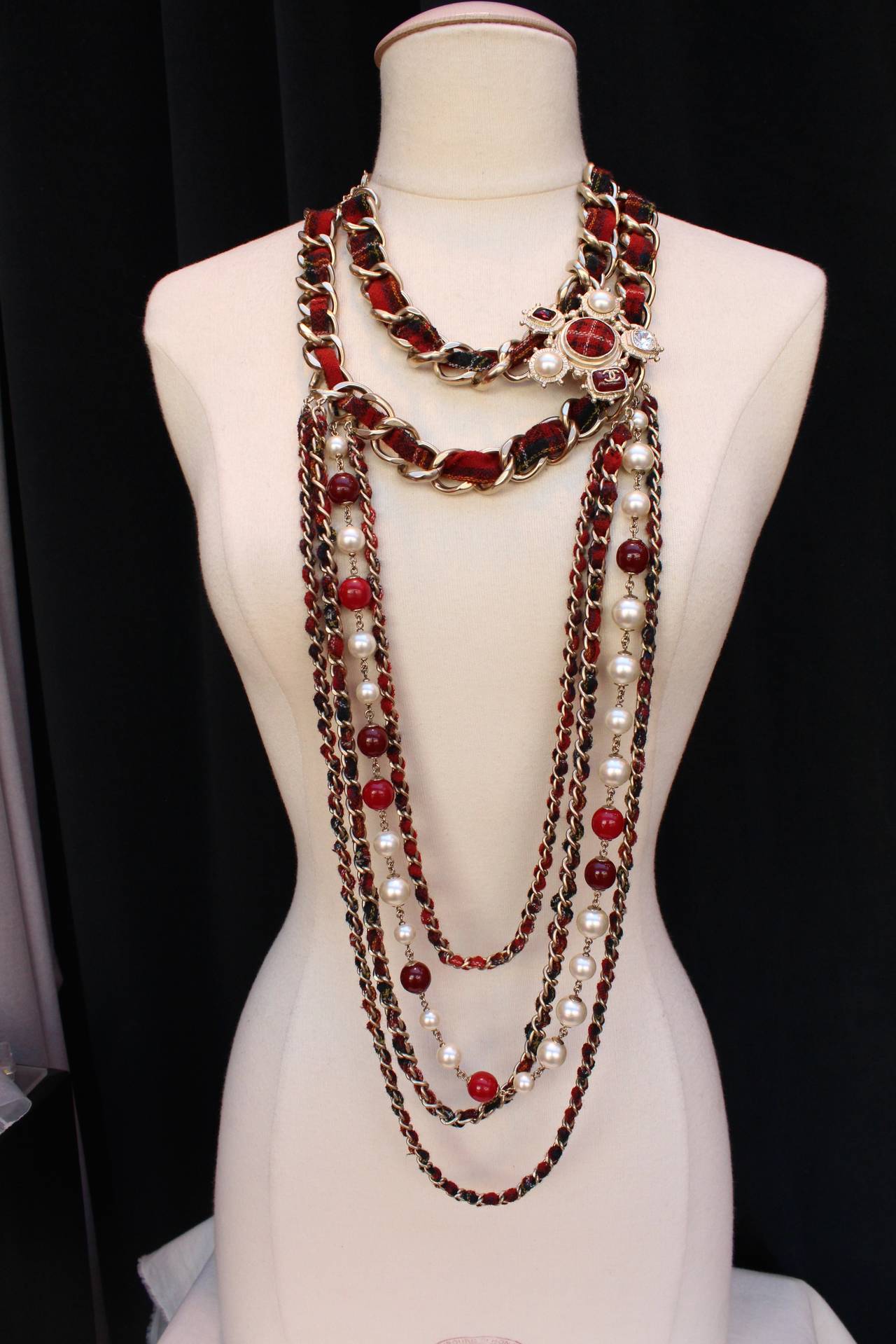 Exceptional multi strands Chanel necklace from the Paris-Edinburgh Pre-Fall 2013 collection, composed of silver metal chain interlaced with red and black tartan strips, red resin beads and faux pearls. 
The necklace is adorned with a cross made of