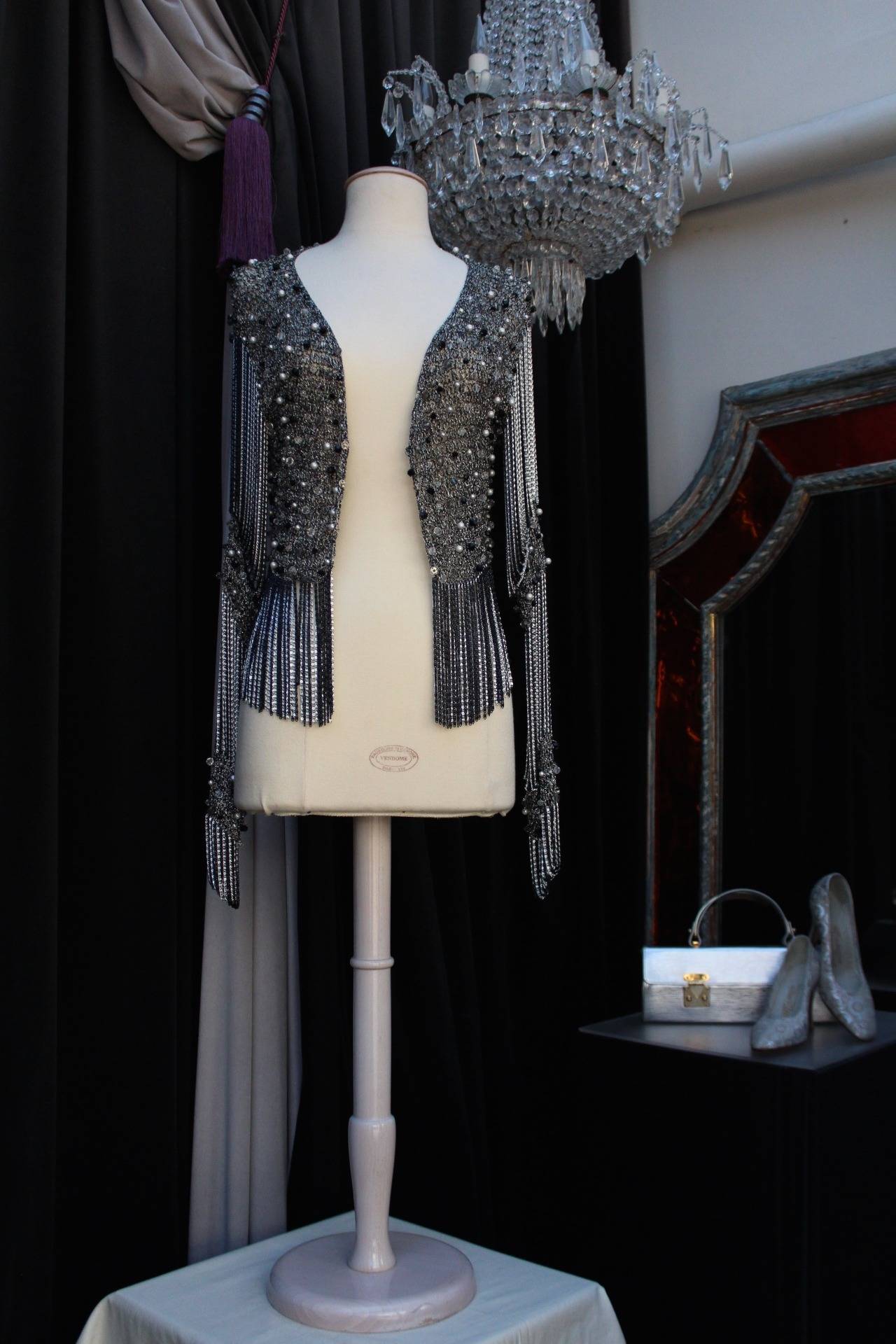 Stunning and Sexy Loris Azzaro handmade crop cardigan composed of black grey lurex embellished with pearlescent white and black beads as well as black and metallic fringing chains on the waist. 

The cardigan consists of long sleeves featuring the