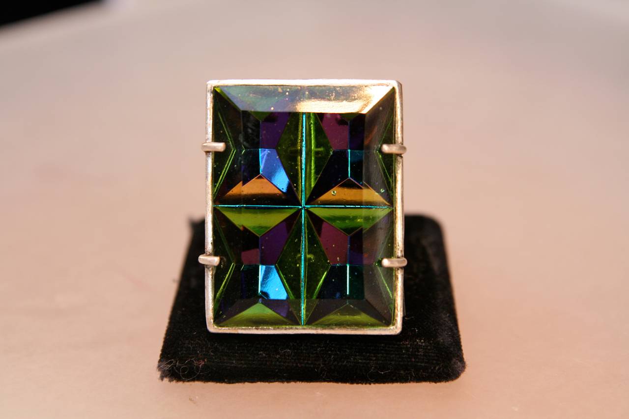 JEAN-PAUL GAULTIER ring from the 1990s composed a rectangular faceted  iridescent green glass set on a chiseled silver metal mount on the reverse. 

This model of ring was showcased in the Jean-Paul Gaultier exhibition at the Grand Palais in