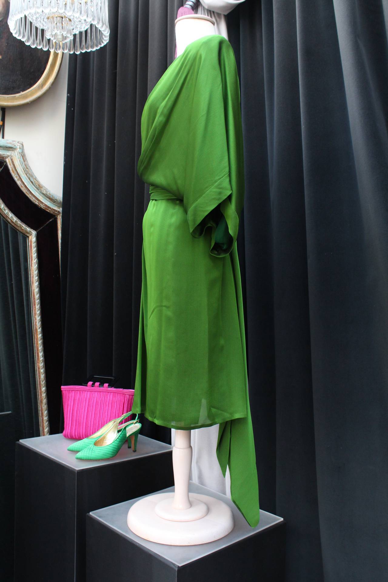 Exquisite knee-length asymmetrical dress by Yves Saint Laurent from his Haute Couture 1990-91 collection, composed of draped emerald green silk. 
The dress features one long sleeve, and one batwing sleeve, as well as a silk belt to be tied around