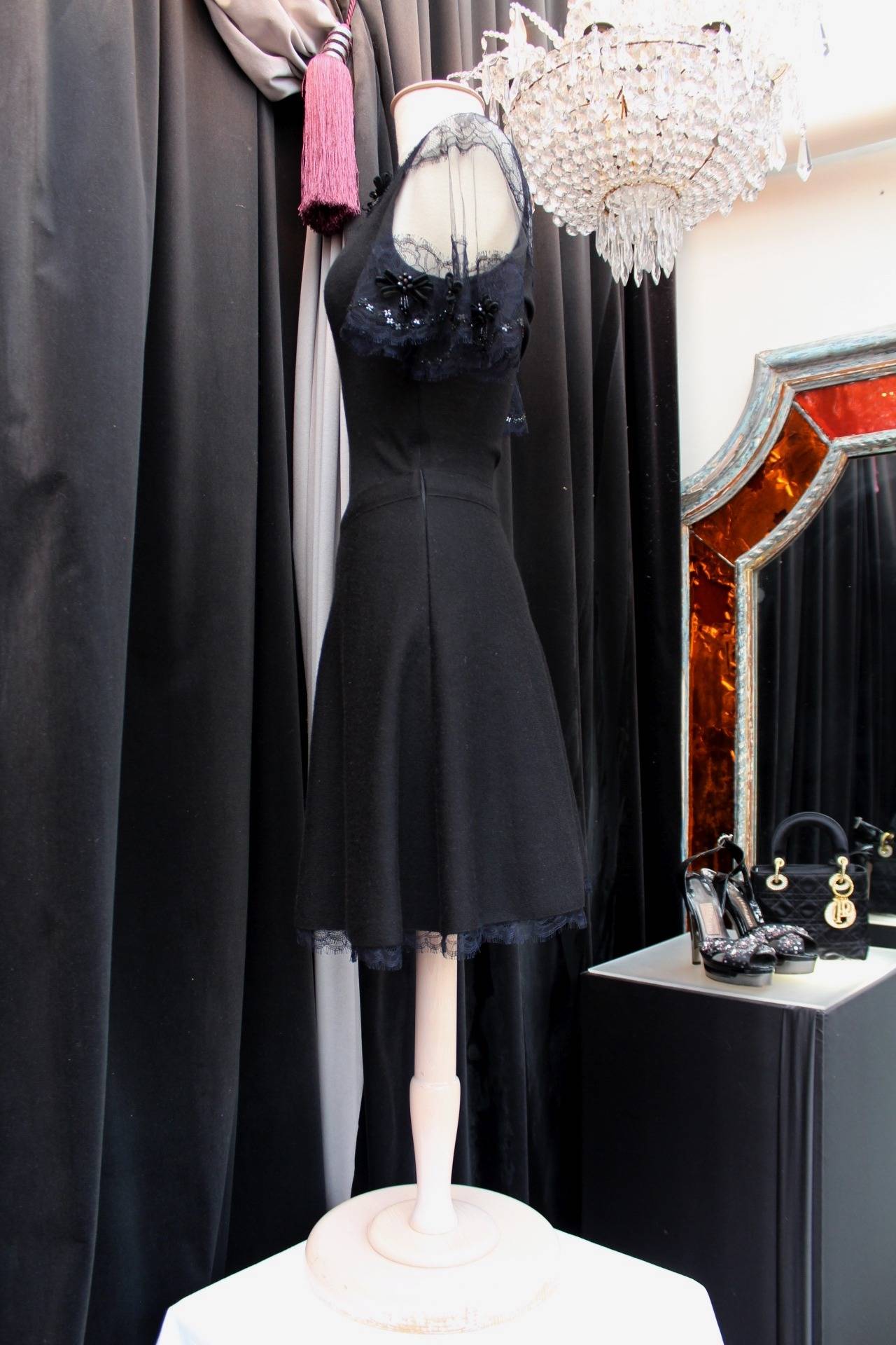 CHRISTIAN DIOR (Made in France) Short sleeves skater dress composed of black woolen cashmere adorned with lace embroidered with bows and beads on the neckline, shoulders and bottom. 

The dress features a waistband and a zip on the left side.