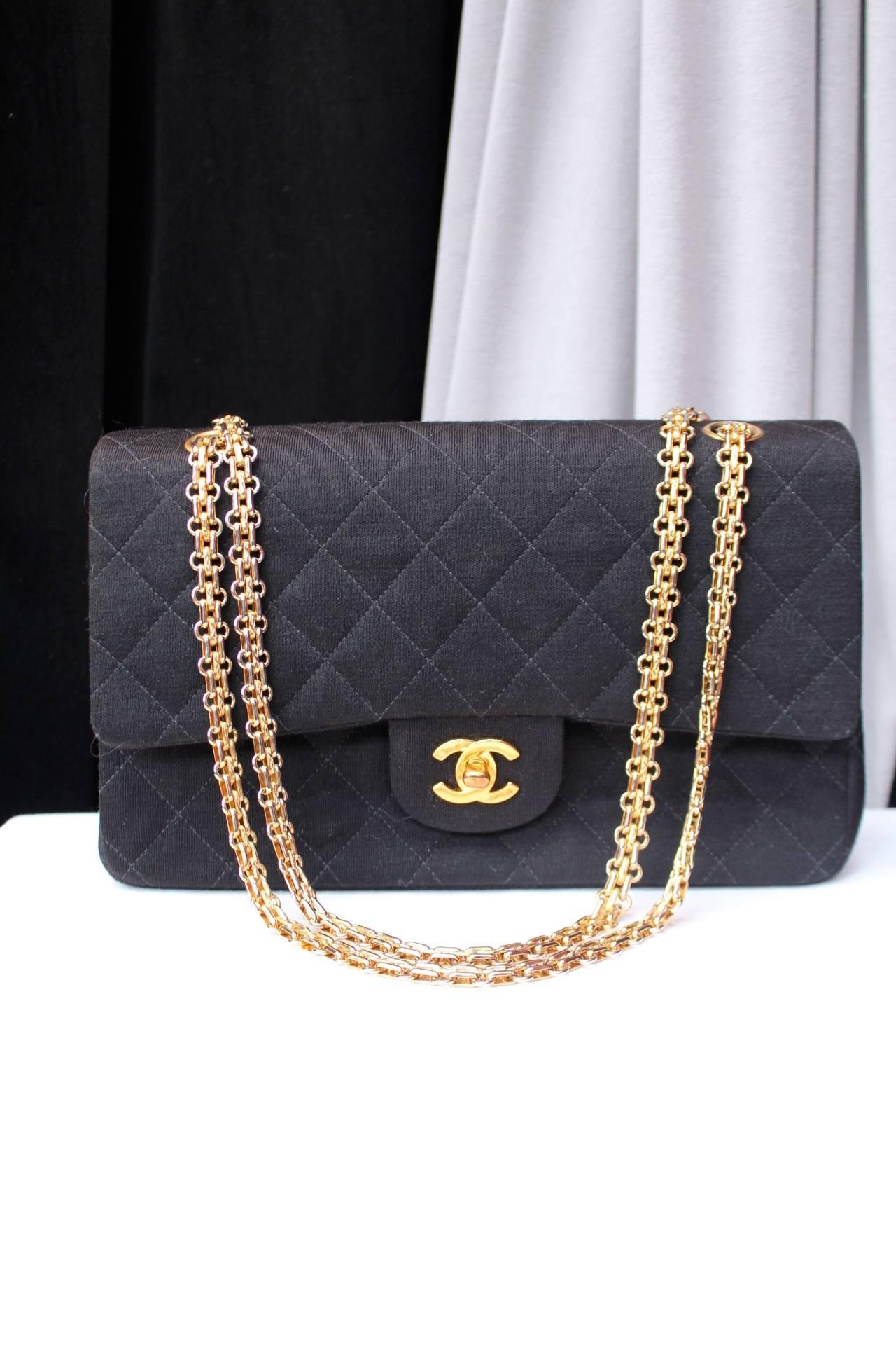 CHANEL Vintage timeless shoulder bag made with black quilted jersey and a beautiful gilt metal chain and a CC logo turnlock clasp. 
Double flap with red leather inner lining. 

One zip pocket in the front flap and two small pockets in the main