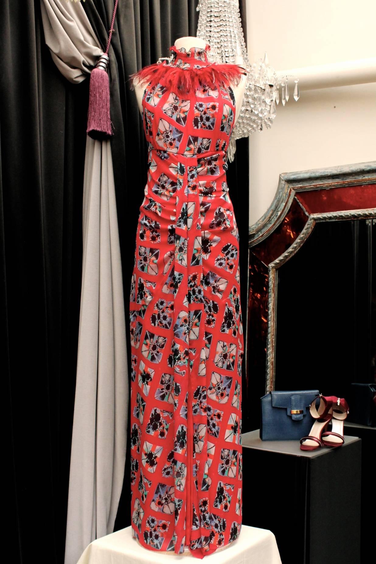 EMANUEL UNGARO (Paris) Long evening sleeveless gown consisting of red silk chiffon with a black, blue, cream and red geometric pattern. The collar is decorated with red feathers and fastens with three silver buttons in the back. Inner lining of red