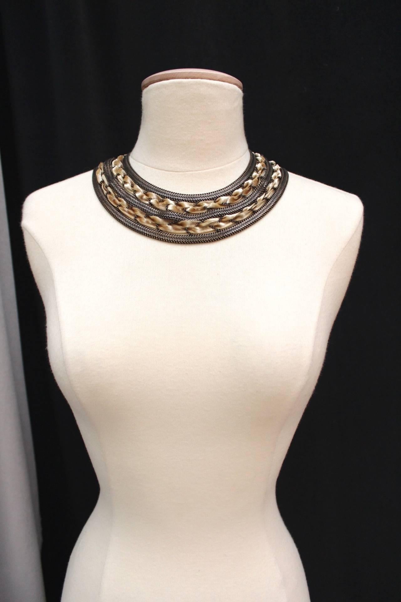 LOUIS VUITTON Short necklace composed of three strands of bronze colored metal interlaced with ivory color silk velvet ribbons braided with thin chains. 

The necklace fastens with a long metal stick, engraved LV. 

Dates from the 2000s.