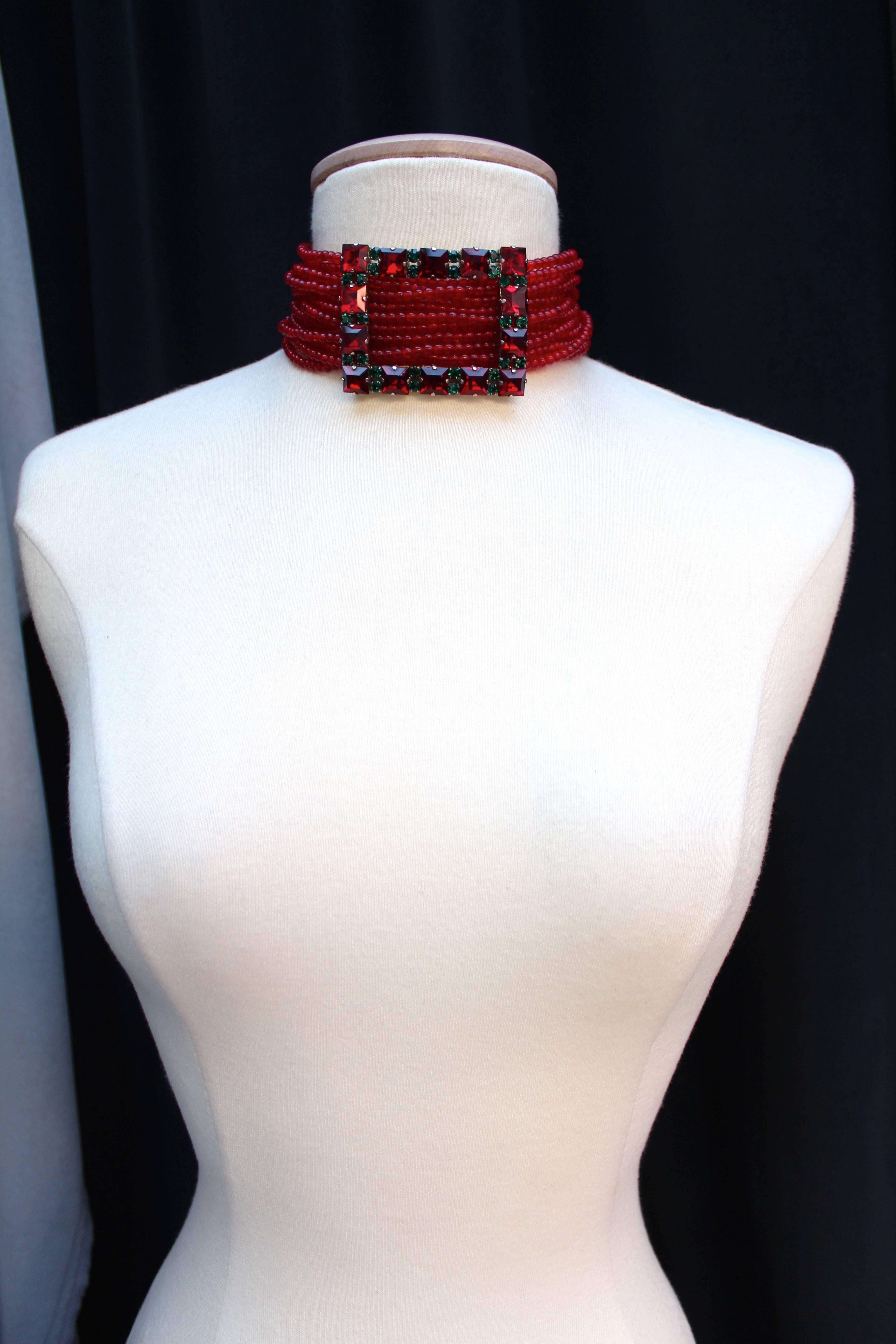 YVES SAINT LAURENT Choker necklace composed of multiple strands of red beads held in the center with a buckle in silver metal paved with red and green crystals. 

The necklace fastens with a S hook in silver metal engraved with YSL. 

Very good