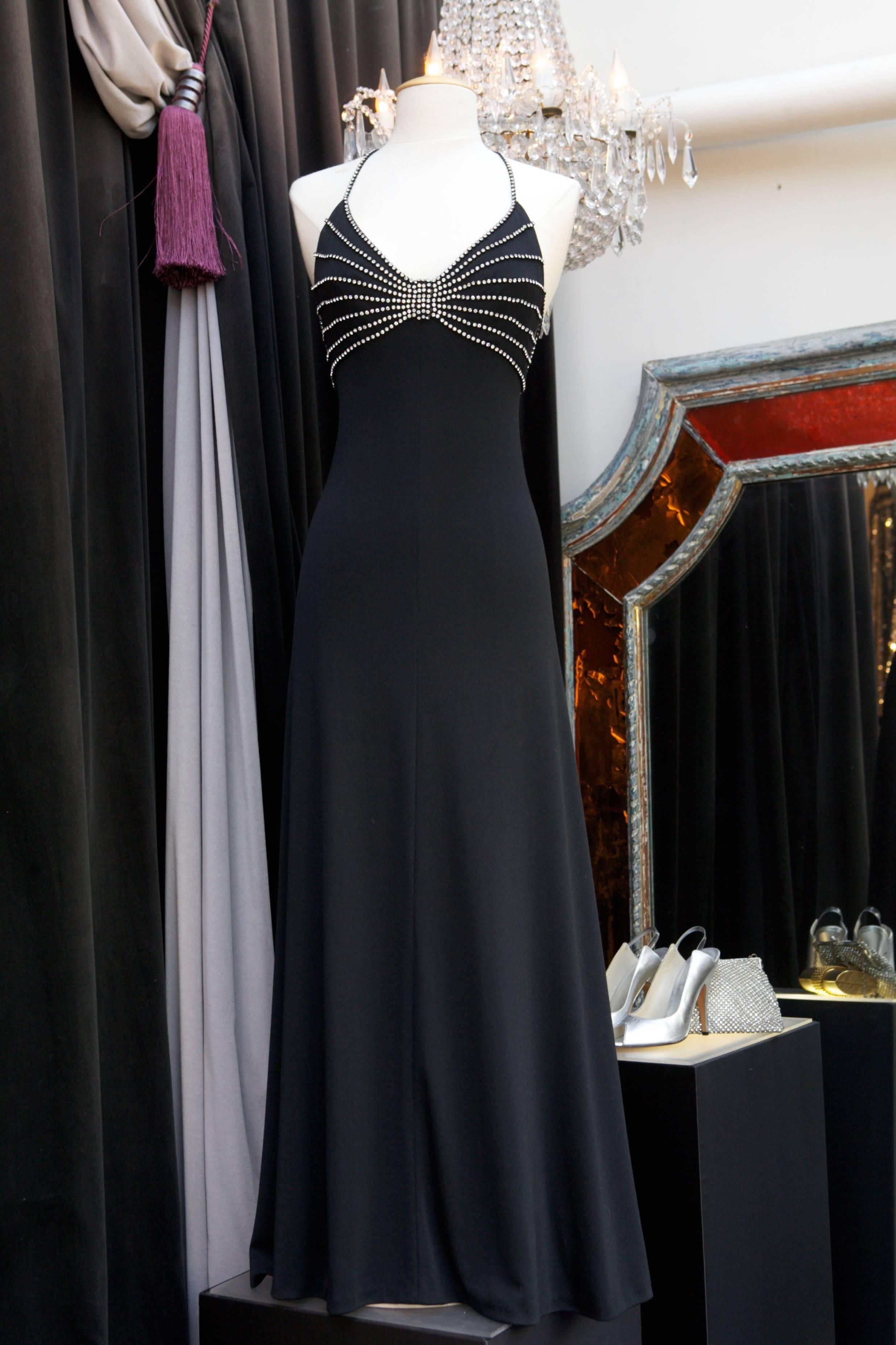 LORIS AZZARO (Made in France) Long and sexy evening gown composed of black jersey adorned with straps and galloons of white crystals on the chest, going all the way at the rear and finish in a flower. 

The dress neckline is very cut out in the