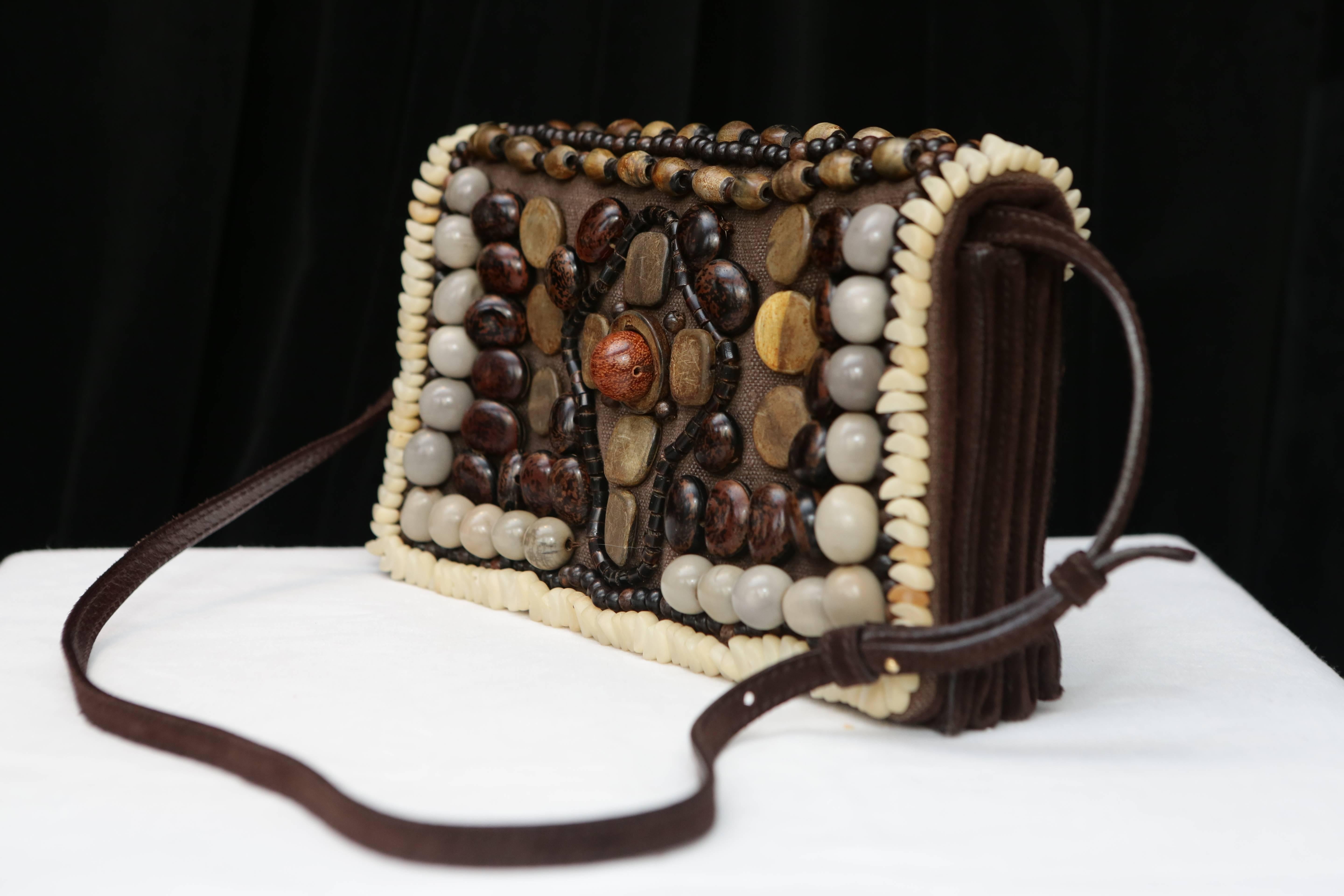 YVES SAINT LAURENT RIVE GAUCHE- Rectangular gusseted bag in brown suede closed by a flap entirely embroidered with stones and wooden beads in a gradation of gray and brown figuring a pattern of a cross.

It has a long brown suede handle for a