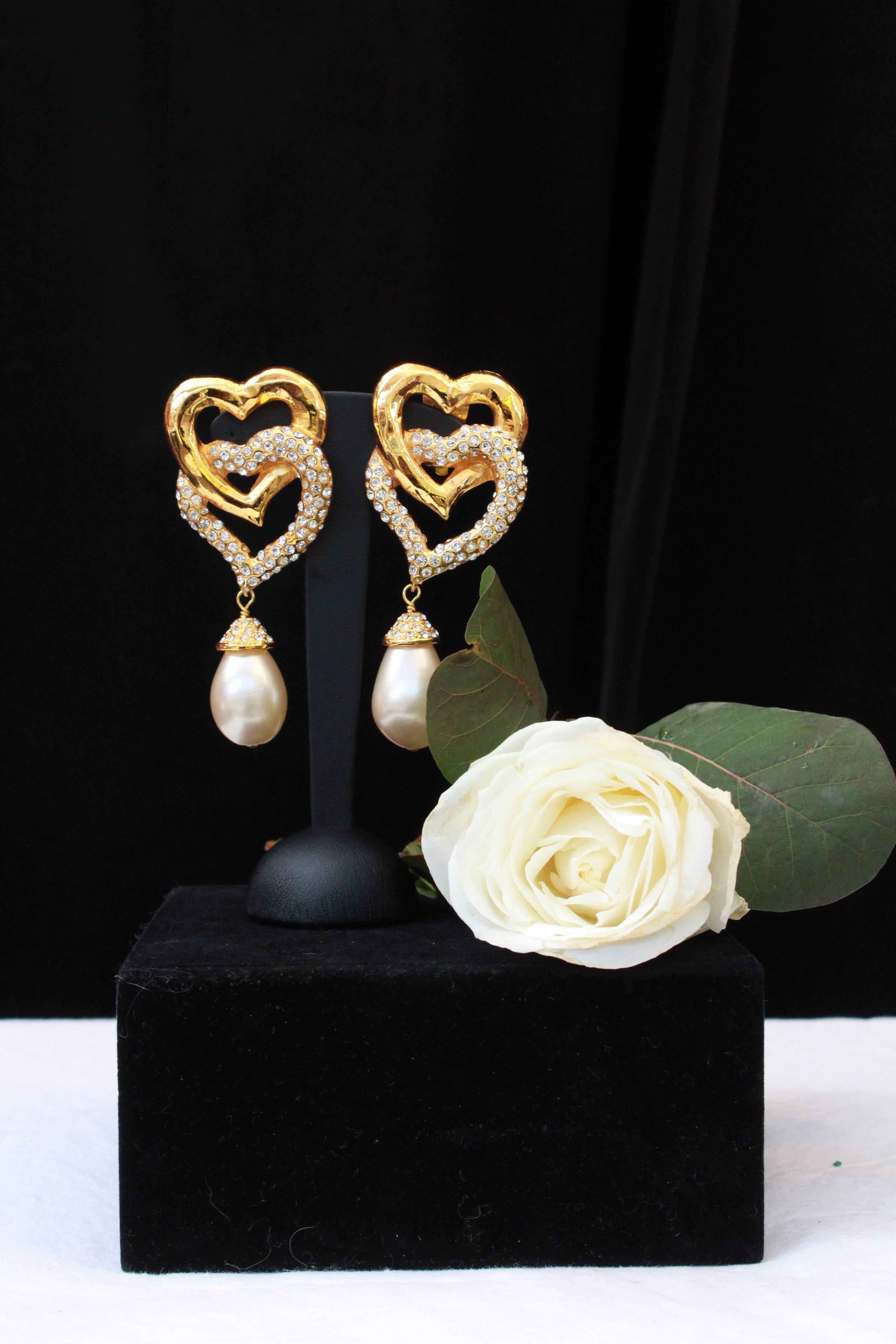 VALENTINO –  Gilded metal clip-on earrings representing two interlocked  hearts , one of them paved with Swarovski crystals. They are further embellished with a pearly teardrop topped with rhinestones.

Circa 1990.

Length 10 cm (4 in); Width 4 cm