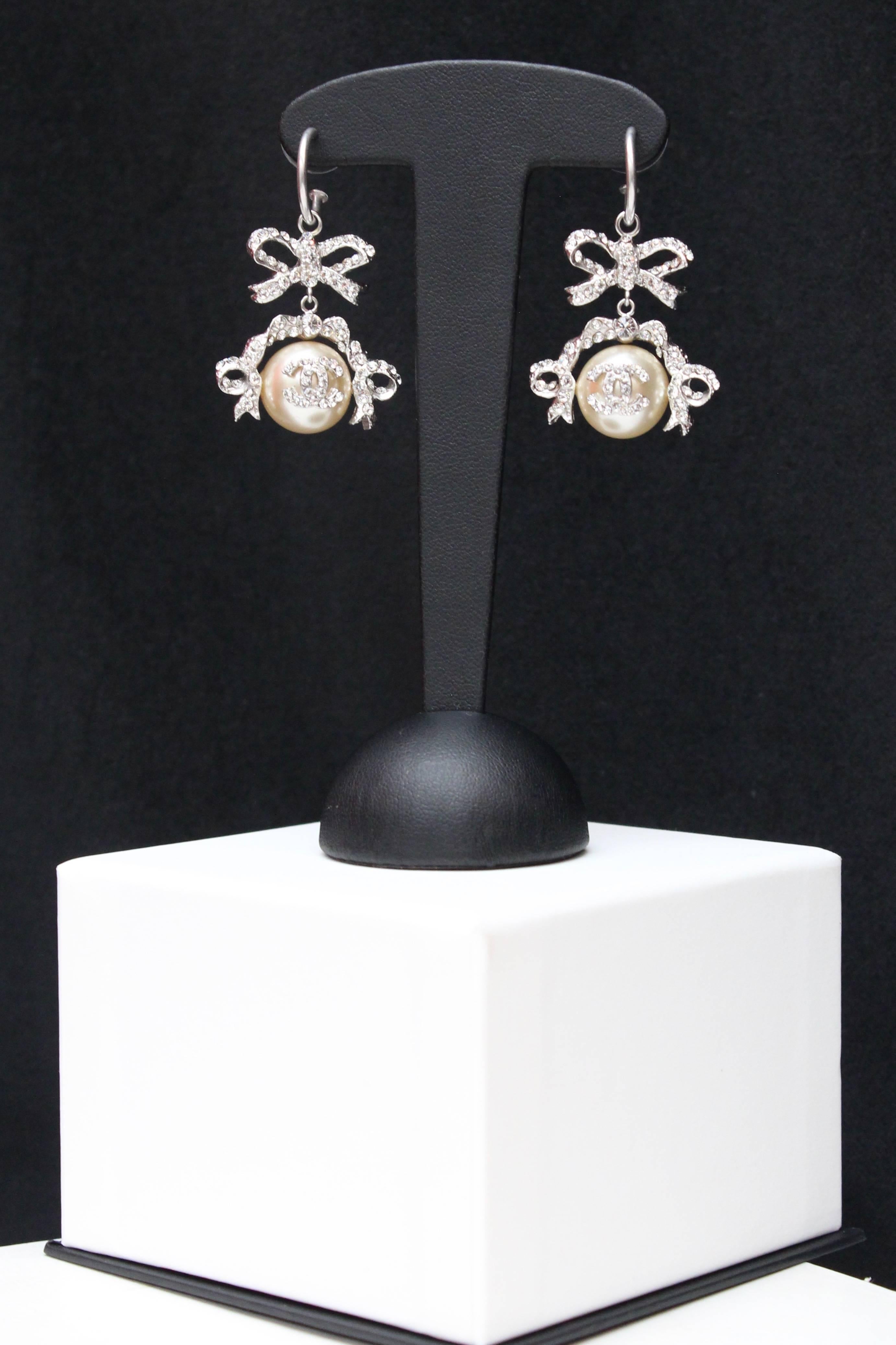 CHANEL (Made in France) Splendid pair of earrings representing a silver plated bow and ribbons set with white rhinestones, and a faux-pearl embellished with the CC logo paved with rhinestones. Signed at the back of the bow.

2004 Spring-Summer