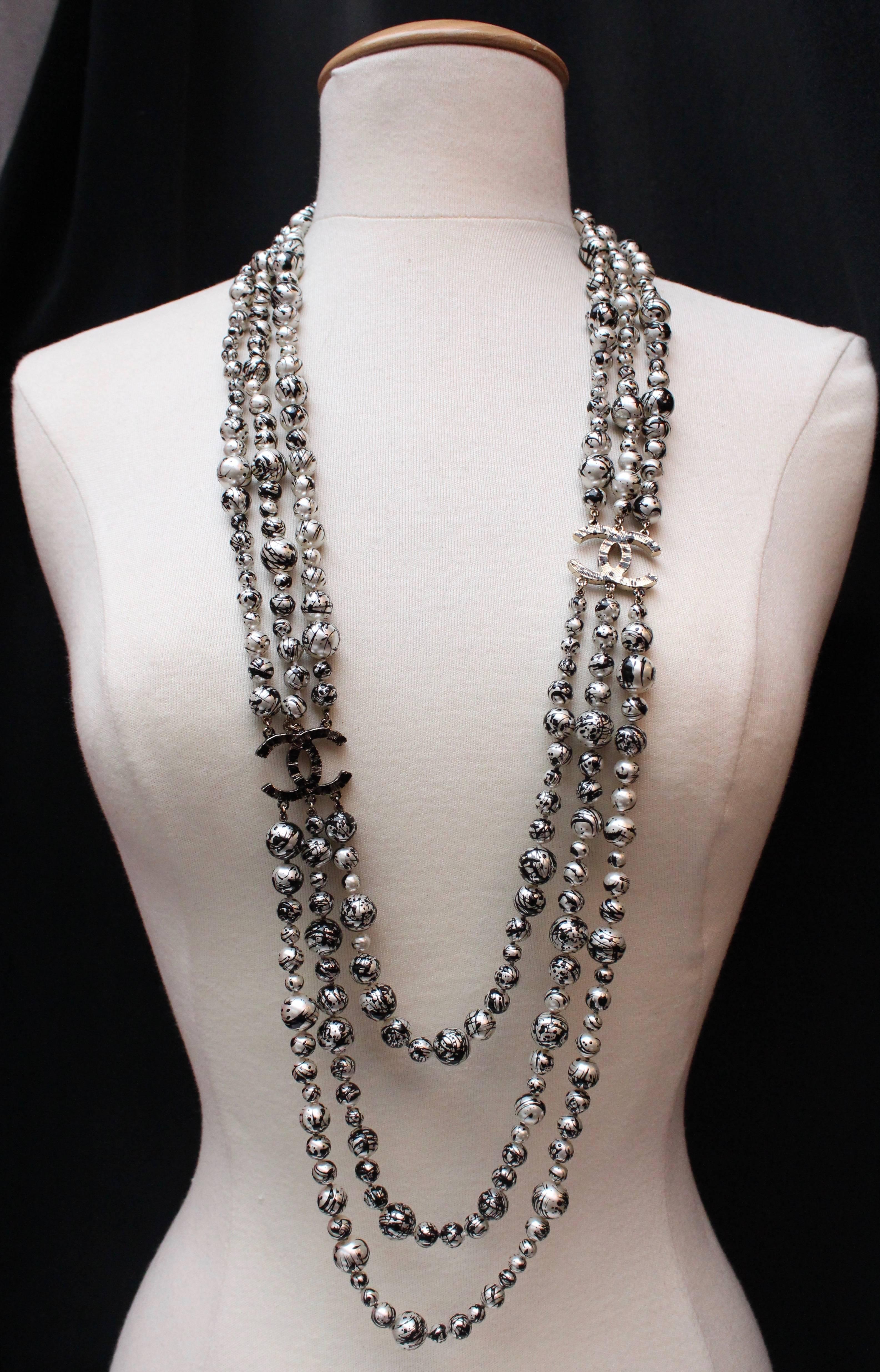 CHANEL (Made in France) Long sautoir necklace comprised of three strands of beads linked by two CC- shaped elements. The different size pearly beads are all decorated with black  random “brush stroke” touches. The necklace is embellished with two