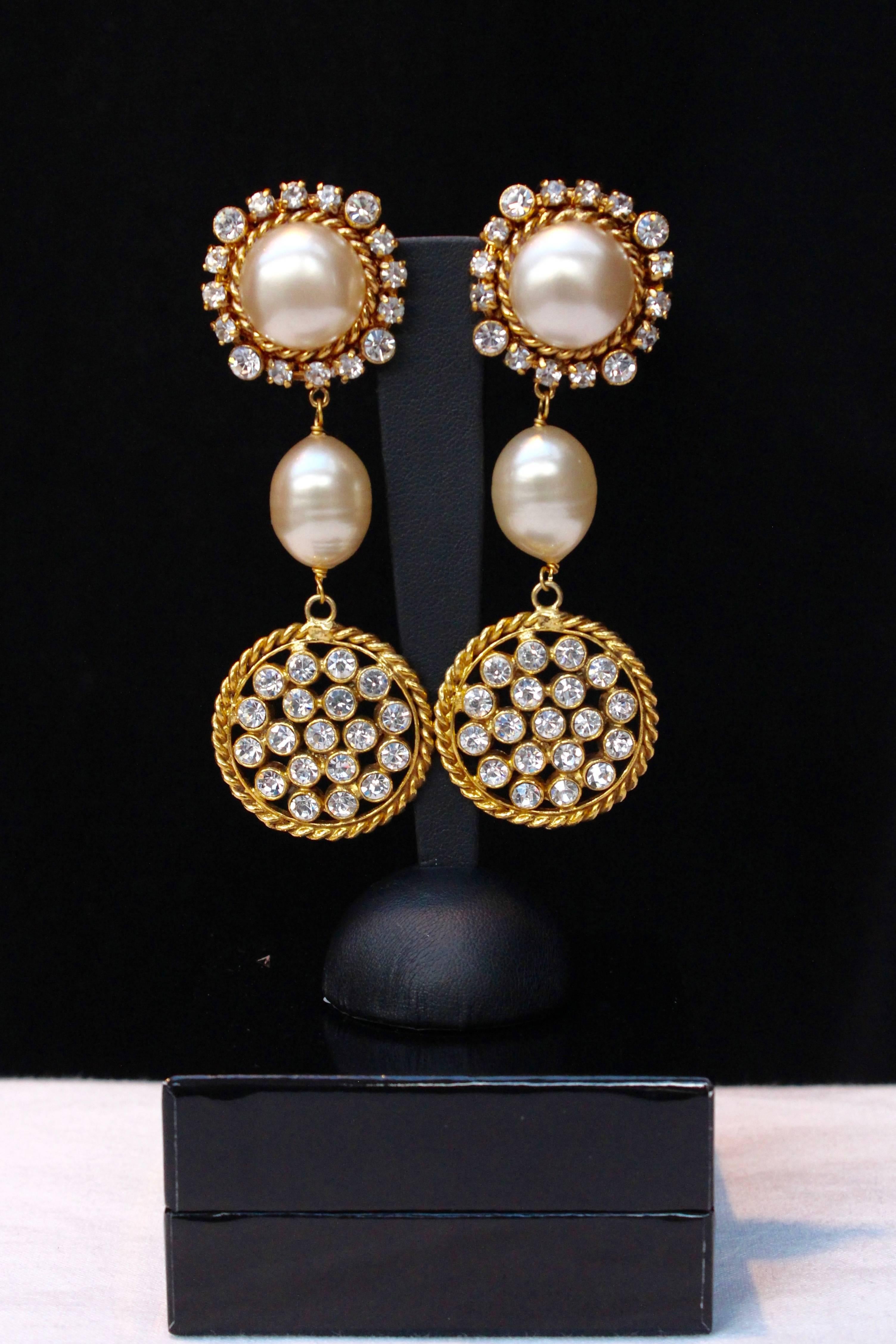 CHANEL (Made in France) Beautiful drop clip-on earrings made of a faux pearl cabochon ringed of rhinestones hanging a faux pearl and a gilted metal hoop paved of rhinestones.

From early 1990 - 1993's

Size : 10 cm ( 3,93 in ).

Very good condition
