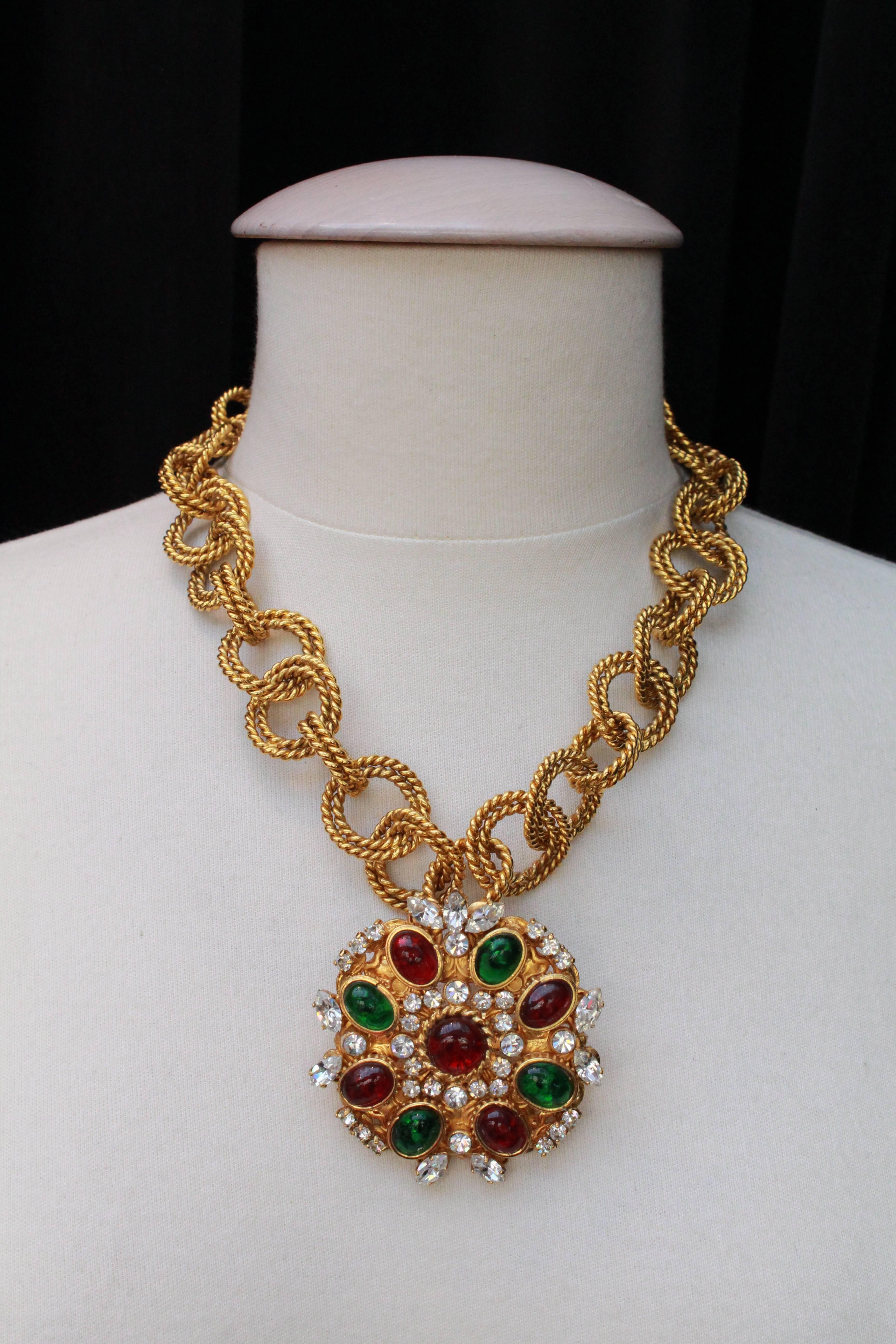CHANEL (Made in France) Short necklace composed of  extra-large gilded metal  chain with cord motif chiseling. A large gilded metal medallion / pendant decorates the center. It is paved with ruby and emerald glass paste cabochons and rhinestones, in