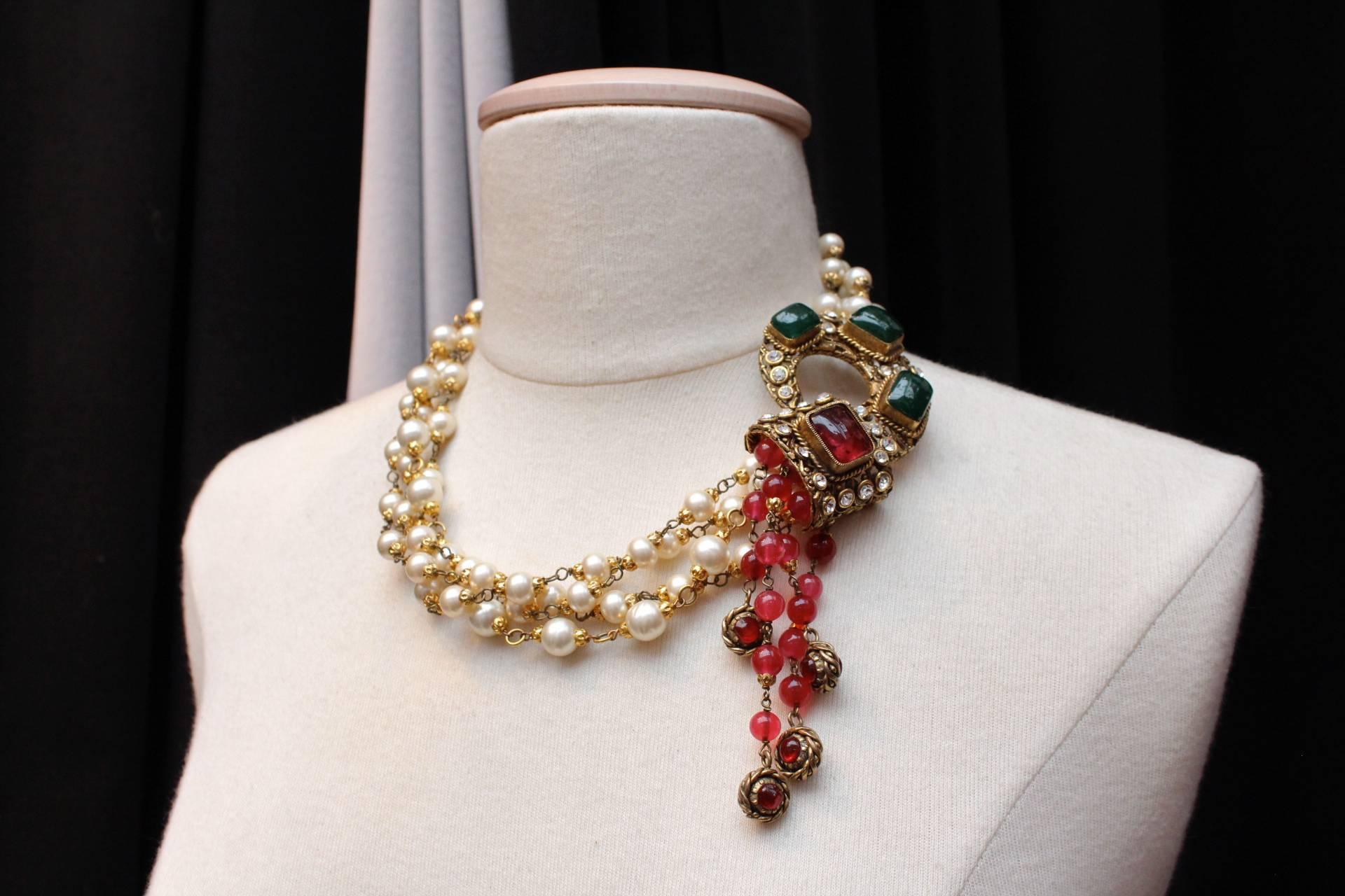 CHANEL ( Made in France) Multi stands necklace composed of faux pearls featuring with a hook clasp in a form of an arabesque in gold metal paved with white crystals and green and red glass paste holding several strands of red glass beads.