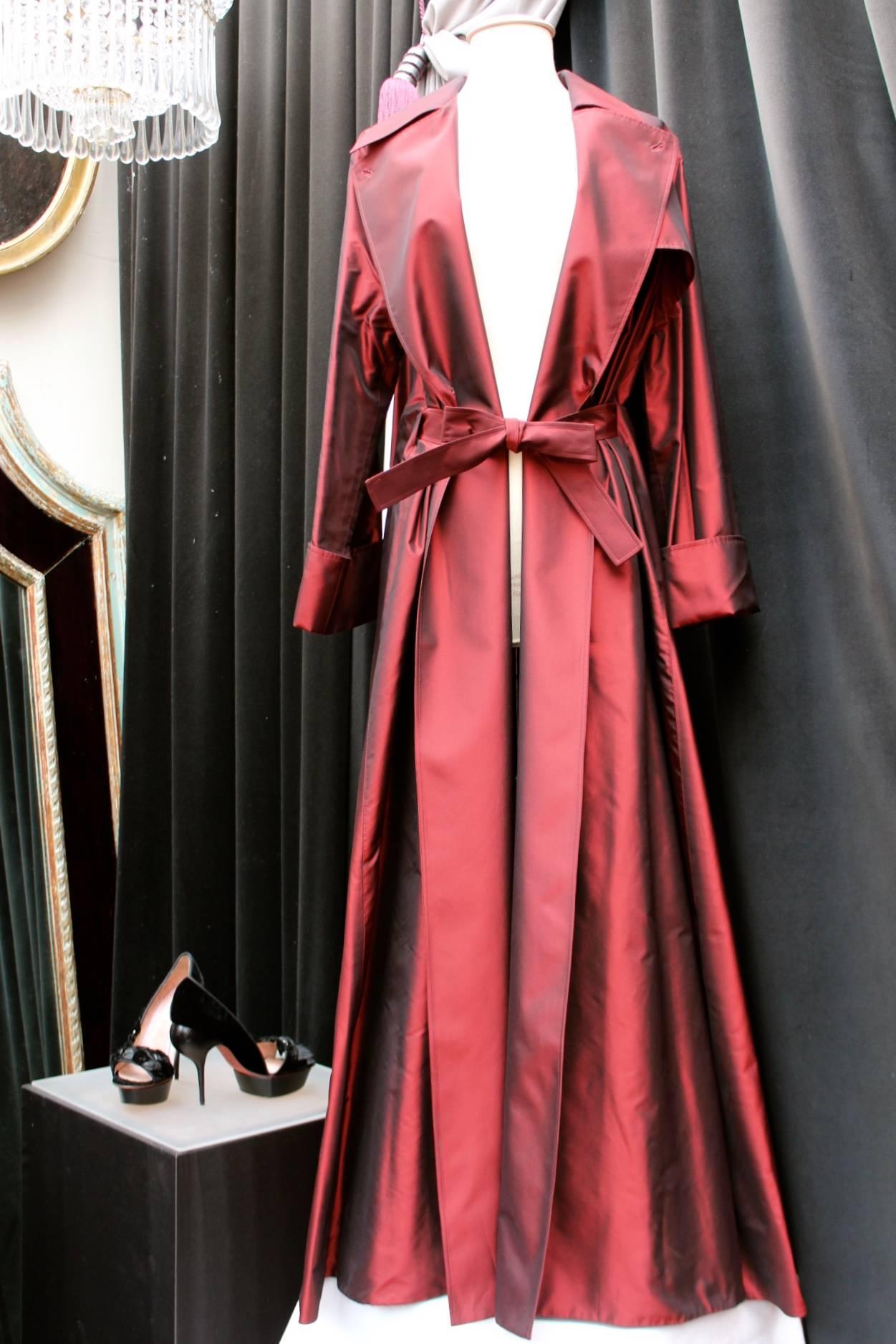 GUY LAROCHE COLLECTION (Paris) Large oversize trench coat in burgundy taffeta fastened with two buttons and a belt of the same fabric. 

The belt goes underneath the trench in the back allowing to show a very dramatic back profile. 

Very good