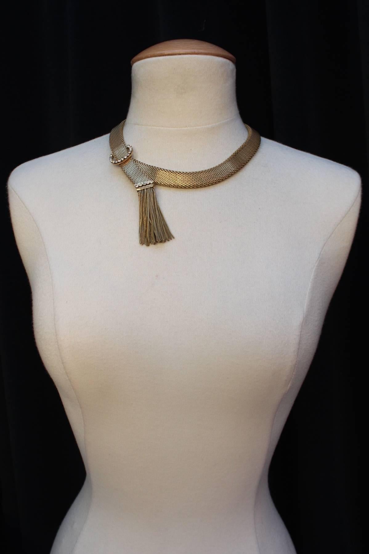 BALENCIAGA (Paris) Rare necklace comprised of gilt metal chain in the style of a snake chain figuring a buckle paved with white crystals and a tassel with crystals and chains.

Piece of 1960s

Signed. 

Very good