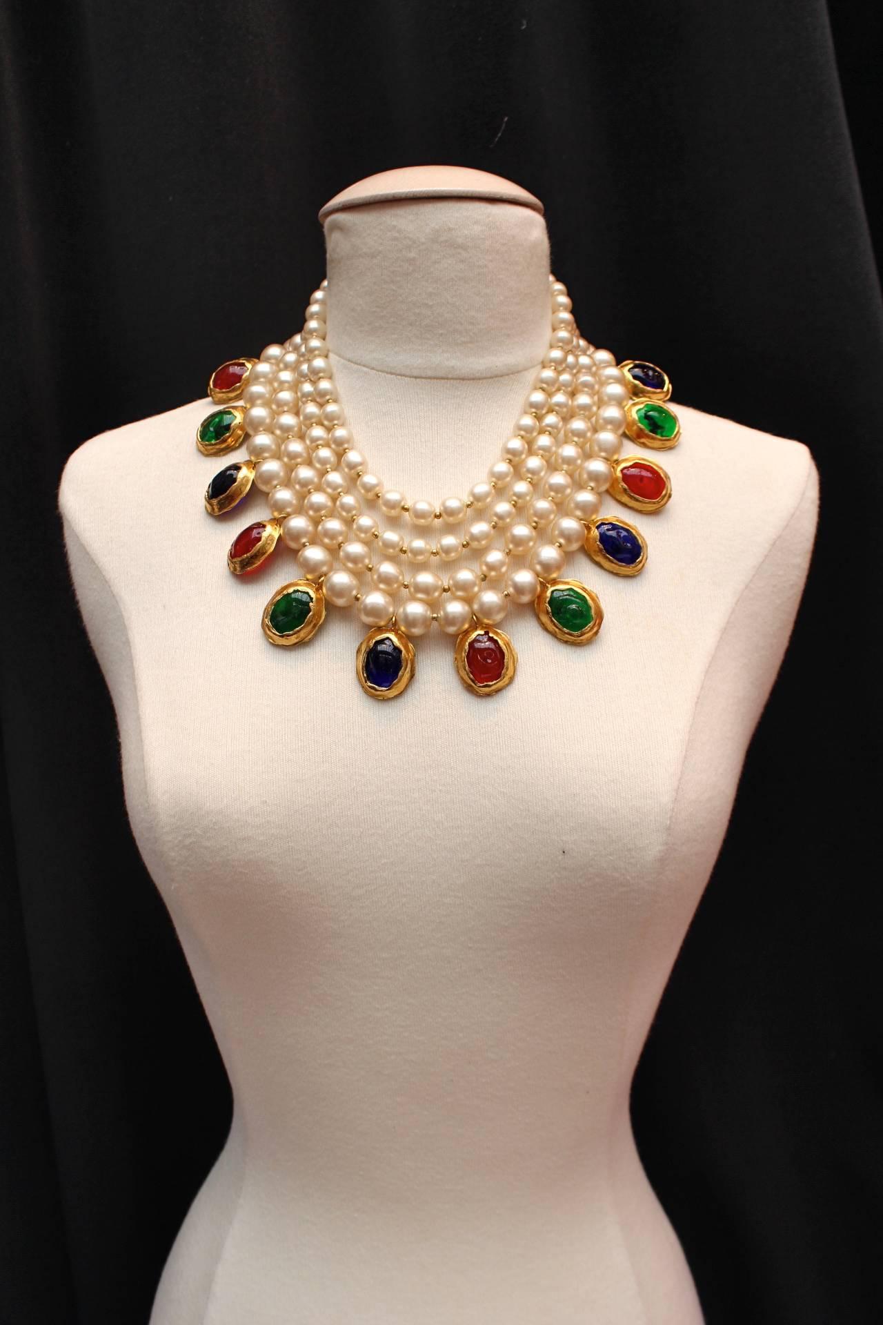 CHANEL (Made in France) Fabulous necklace comprised of four strands of faux pearl holding several cabochons of red, green and blue glass paste circled by hammered gilt metal. 

The necklace fastens with a two hooks clasp.

This piece has been