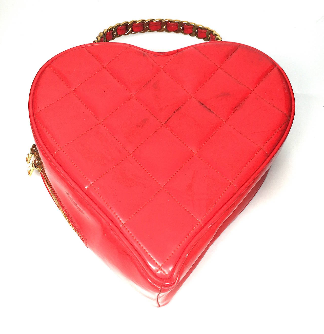 Rare, vintage Chanel quilted red patent leather CC logo heart handbag with gold-tone chain handle and top zippered closure. Features red lambskin interior and heart shape. The bag is in good vintage condition with mild to moderate color transfer on