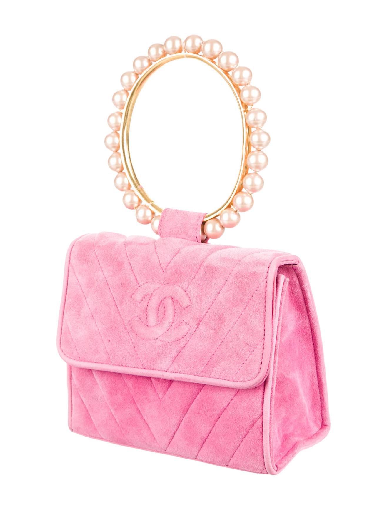 Pink suede Chanel handbag with with gold-tone hardware, contrasting pearl top handle, stitched CC logo at front, black leather lining, zip closure pocket at interior wall and snap closure at front flap. Serial number reads 1988006. Includes