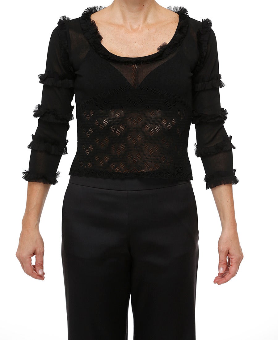 A very feminine Chanel knit viscose top with lacy diamond pattern and scalloped hem.  The neckline and long sleeves are trimmed with soft ruffled silk mesh ; Small black CC logo encrusted with 16 tiny black crystals on front left above hem.  Wrinkle