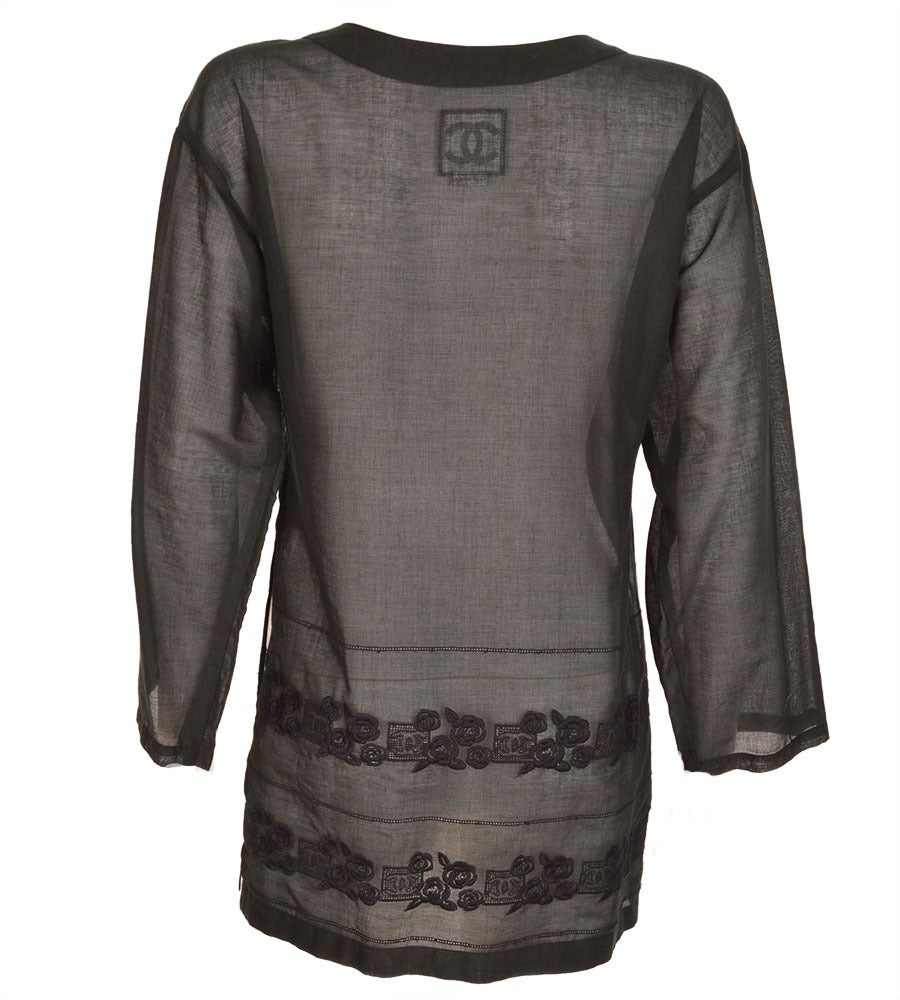 This beautifully made long sleeve collarless black tunic is a part of CHANEL’s Sport Line.  The silhouette has a neck opening with 3 buttons, features a double row of subtle black embroidered camellias and CC logos interspersed with 3 rows of lace