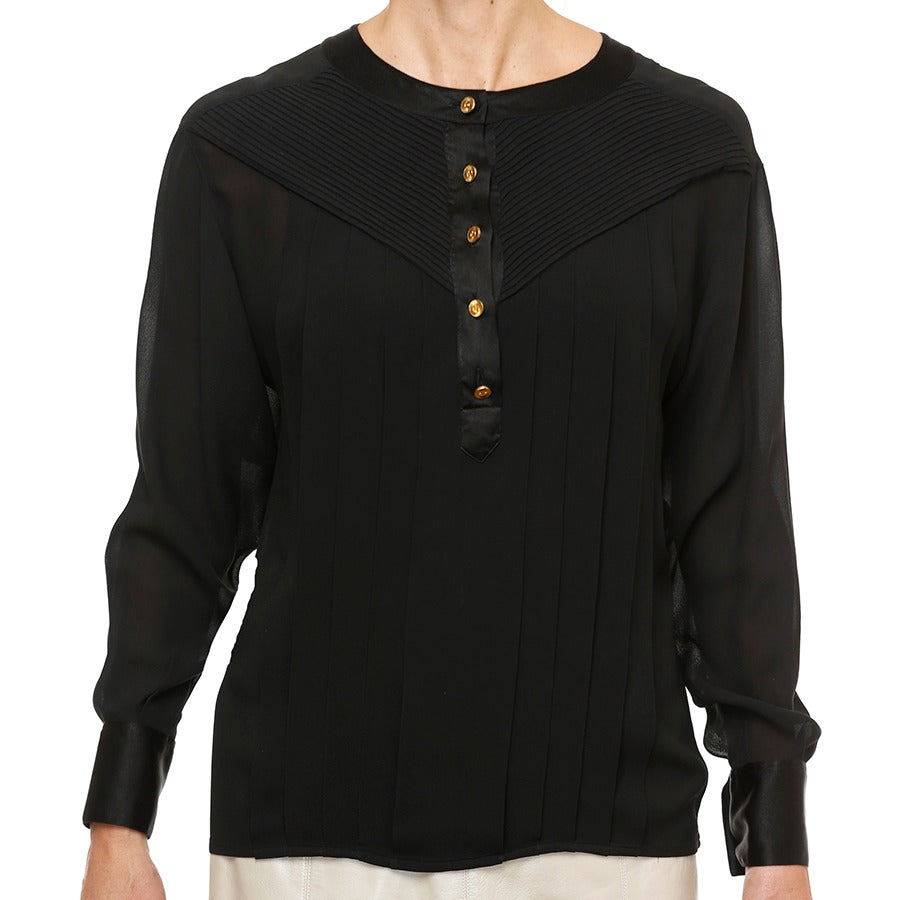 This collarless “black on black” silk crepe with satin trim is typical of CHANEL’s inimitable workmanship.  The raglan silhouette features 22 mini stitched down diagonal pleats (on each front side of the neck opening) for fit and vertical pleats for