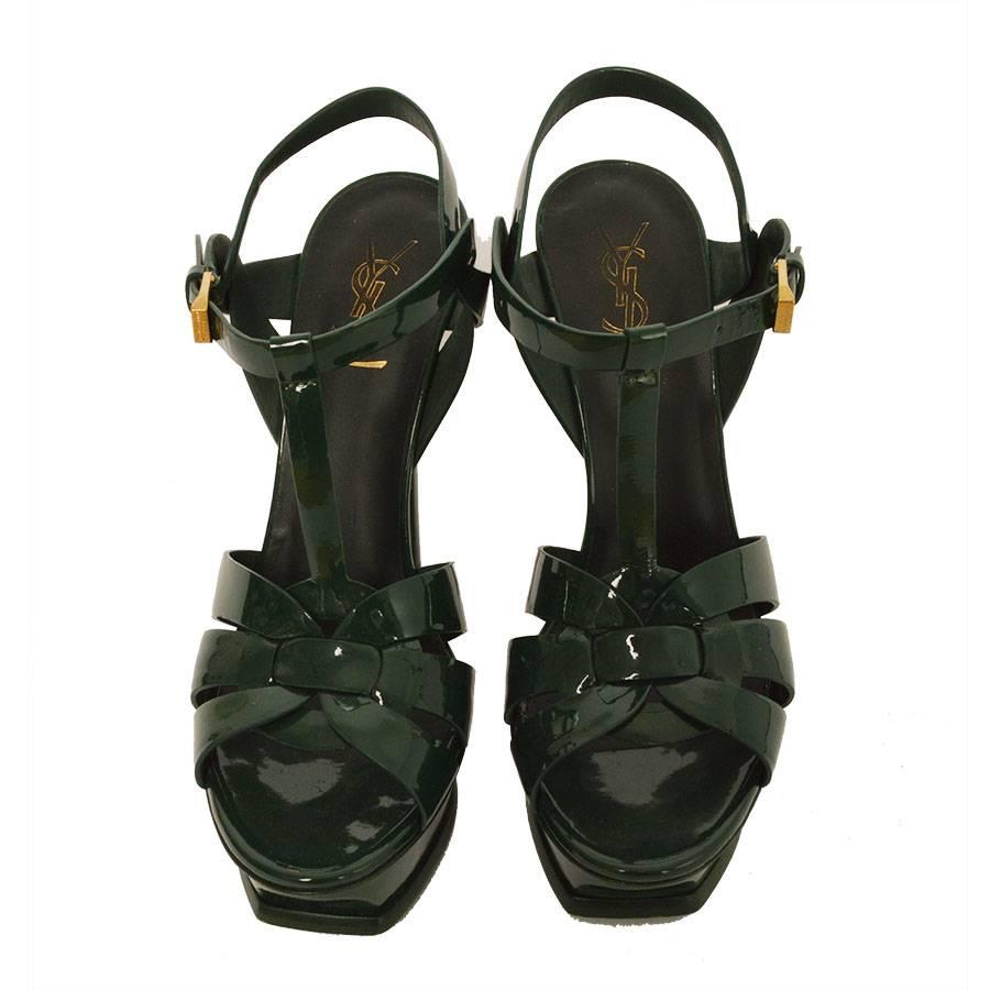 YSL, Yves Saint Laurent Tribute green patent leather platform pumps.  The platform is beveled and paired with intertwining straps in a glossy patent leather to create the iconic YSL Tribute sandal. A refined stiletto heel and adjustable ankle strap