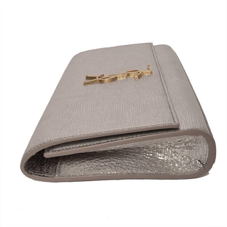 YSL, Yves Saint Laurent Cassandre clutch bag in metallic silver. Sleek lines and understated hardware offer elegant, chic style. Metallic, crinkled goatskin with gold-tone hardware. Flap top with YSL lettering. 

- Approx retail price: $1440.00
-