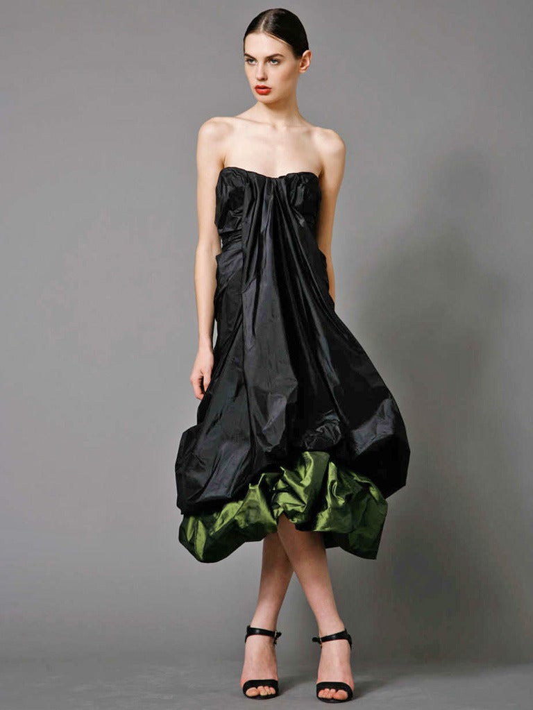 Vestido de noche de tafetán de tejido bicolor negro y verde petróleo, sin tirantes, de Alexander McQueen. Bustier con detalle central drapeado y fruncido en toda la prenda. Dobladillo en globo con capa de contraste debajo. Top de corsé oculto con