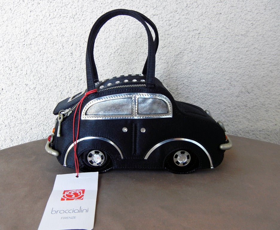 Brand new w/tags Braccialini handbag in the shape of a Fiat car. Fashioned of black satin fabric with dual zipper closure, bumpers, headlights, handles, and rims. Lots of wonderful, whismical and adorable details! Lined interior with contrasting