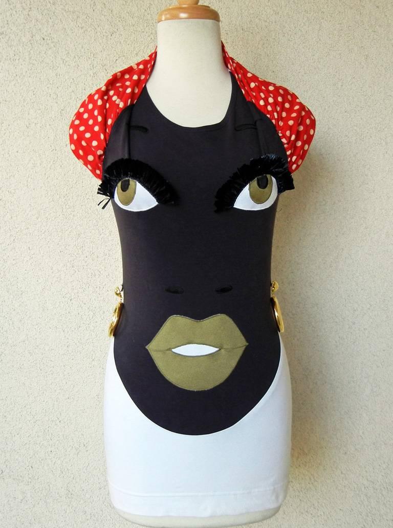 Early1990's graphic ethnic folk art tunic top designed by Franco Moschino.  Fashioned of 100% stretch cotton and made in Italy.  Consists of a halter style with full face, bodice including eyelashes, eyebrows  and hanging gold tone