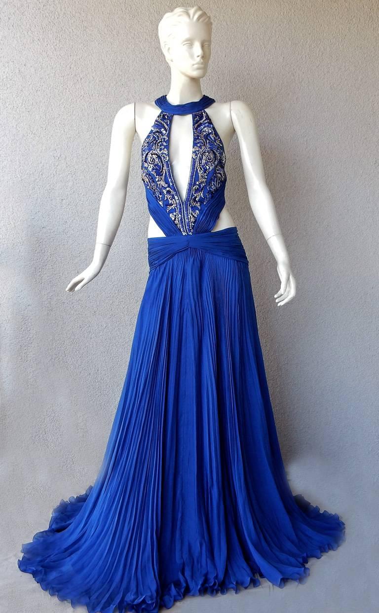 Striking Roberto Cavalli sapphire blue silk chiffon gown.  Bodice boasts a plunging neckline with side cut-outs in a secured style bodysuit.  Elaborate  bead work and hand pleating further enhances the detailed bodice. Long full flowing skirt.  