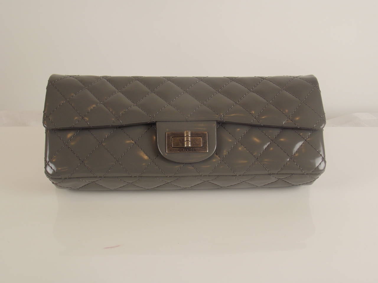 This unique Chanel grey clutch is a sample produced for the runway.  The clutch features a turn-lock closure, a chain strap, two inner pockets, a mirror and glossy patent leather quilted in signature Chanel diamond stitched pattern.  