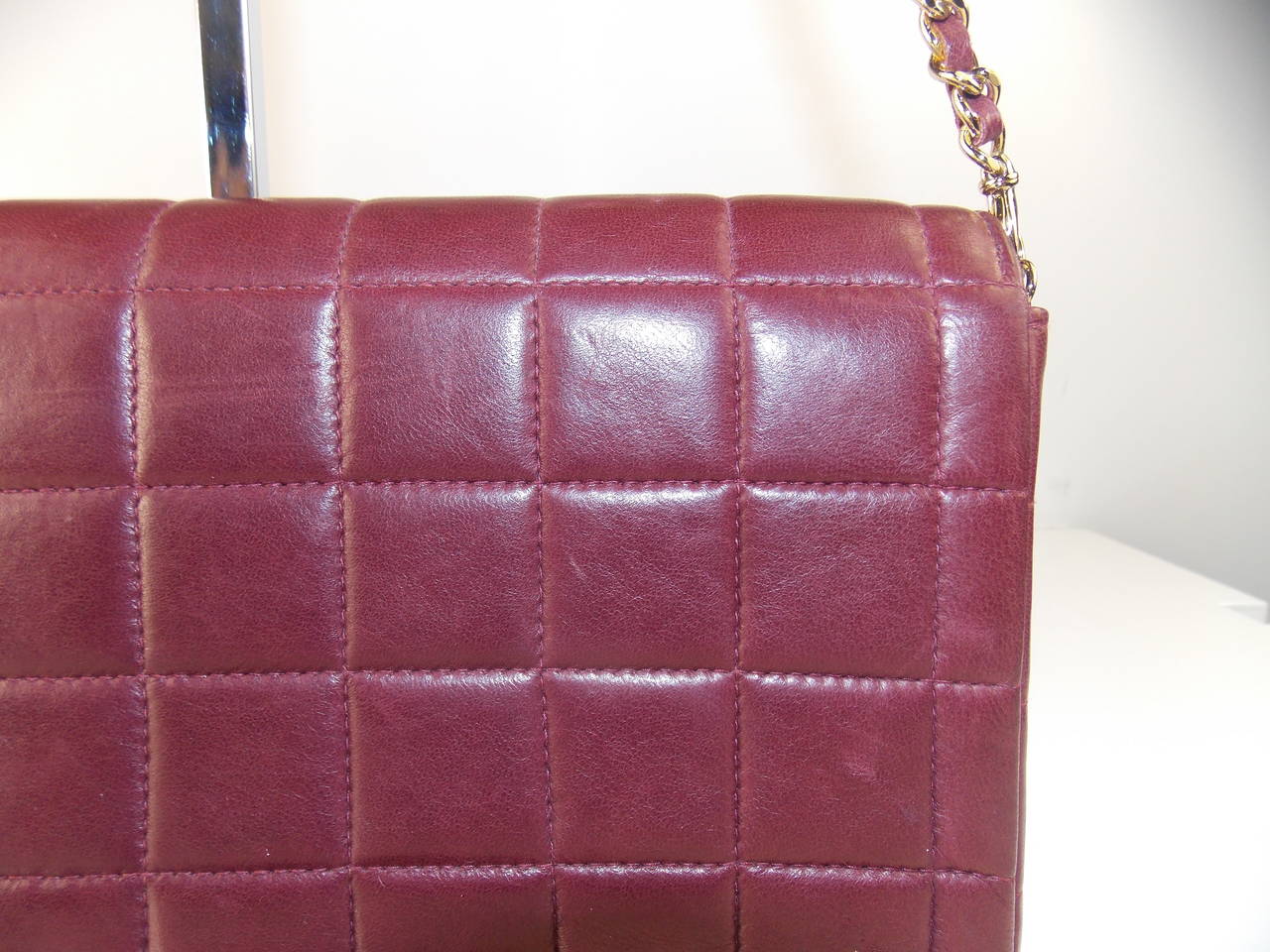 This exquisite bag features a CC gold button closure, a chain strap, two inner pockets, lambskin burgundy leather quilted in signature Chanel square stitched pattern.  