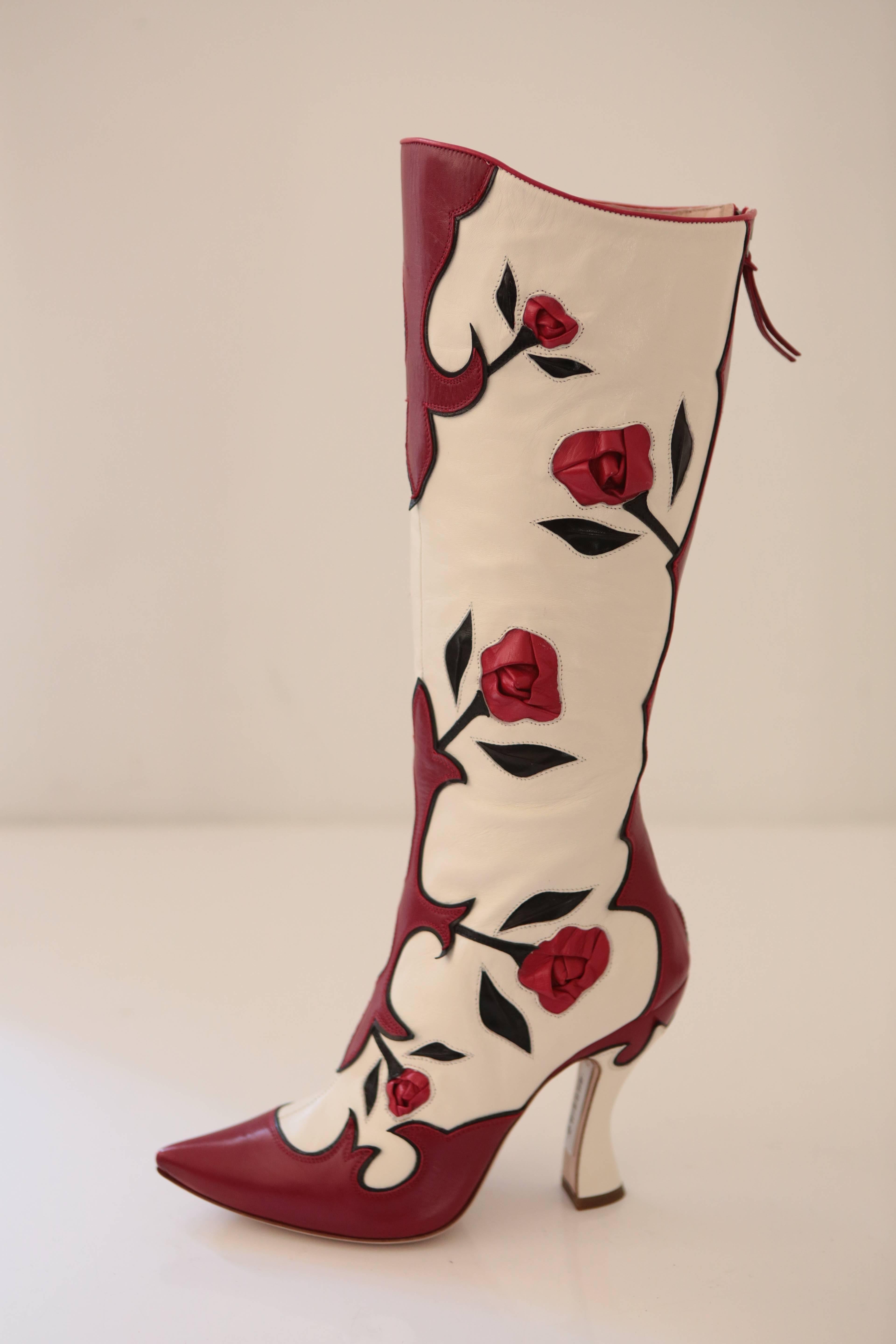 The perfect cure to an all black outfit, these knee high boots feature leather adorned roses and panels of red that truly pop. Sitting on a stacked heel of 4