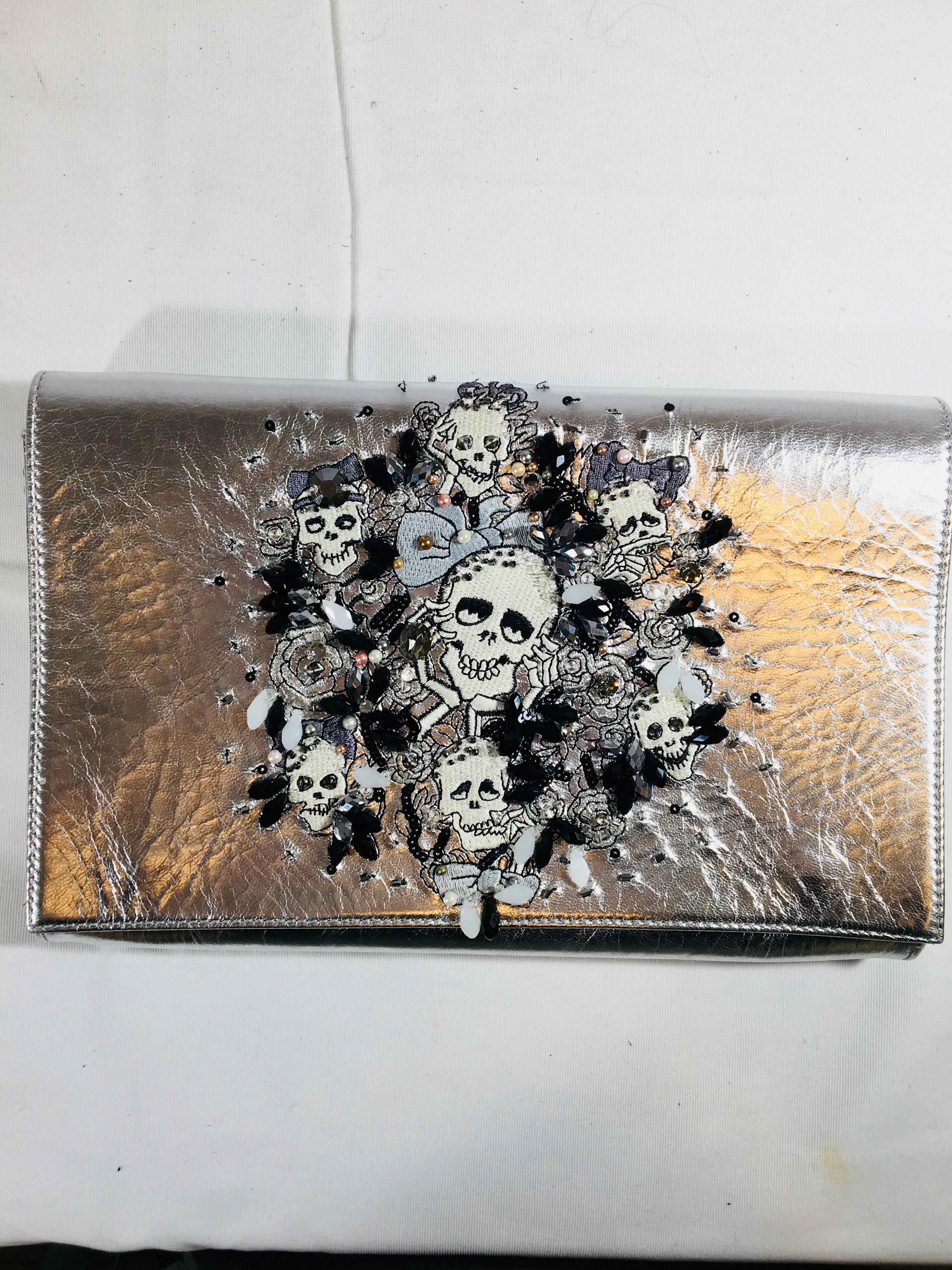Preciously Paris Skull Shoulder Bag.
Silver Skull and Rose Embroidered Bag with Crystal and Bead Details. Flap Button Closure with Removable Silver Chain Strap.