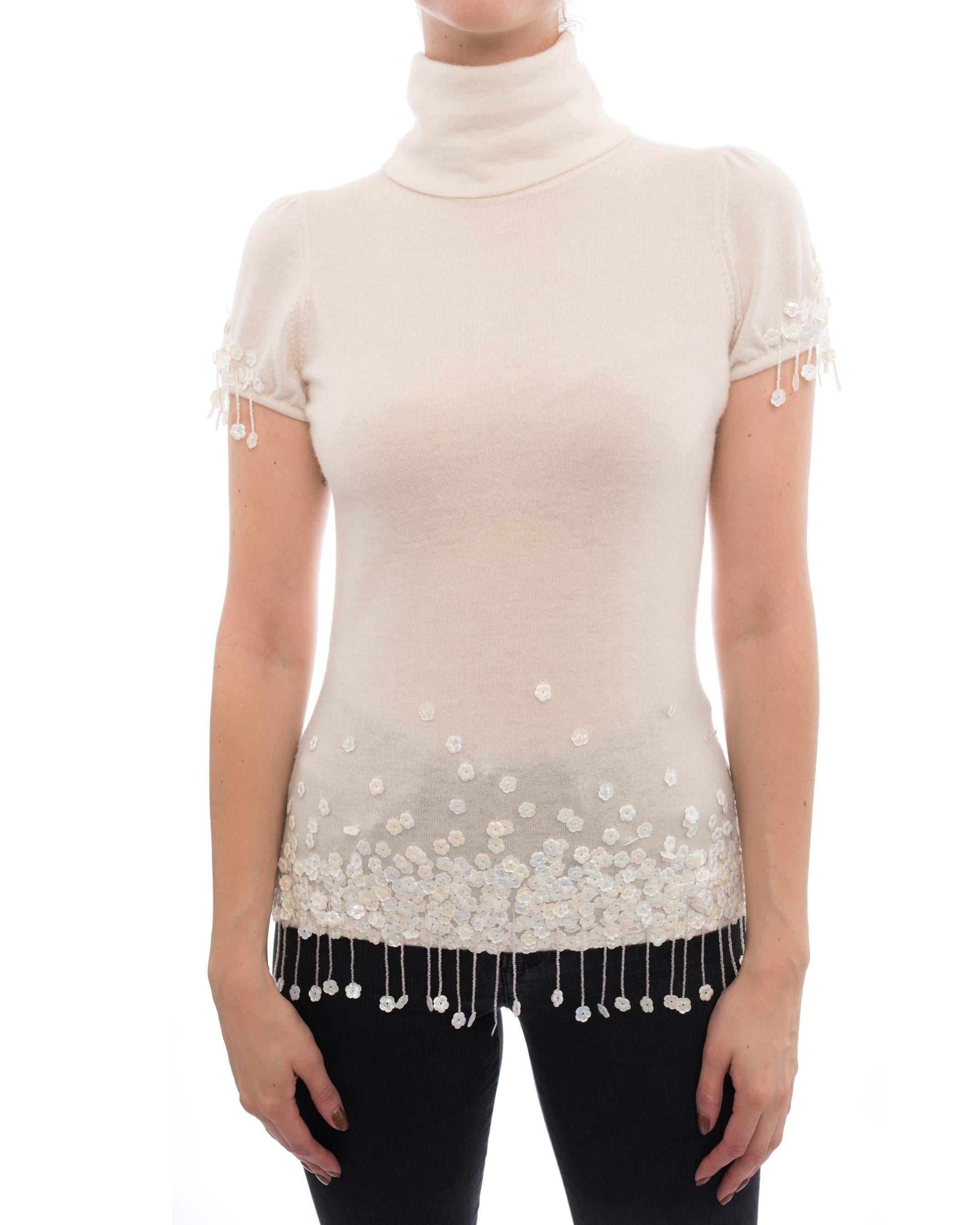 Chanel 04A Ivory Cashmere Knit Top with Sequin Bead Fringe.  Black and white enamel buttons at back neck, high funnel neck, short cap sleeves, iridescent floral paillettes with seed beaded fringe. Marked size FR 38 (USA 6).  To fit 34” at bust, 15”