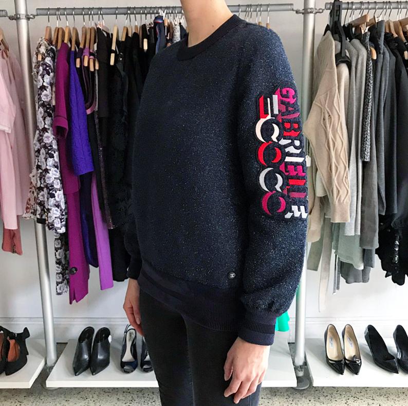 Chanel 17B Navy Textured Shimmer Gabrielle Coco Pullover Top.  Original retail price tag of $3550 included.  Long sleeve pullover sweatshirt with ribbed neck, cuffs, hem.  Gabrielle Coco applique in red, grey, magenta, white at left arm.  Side