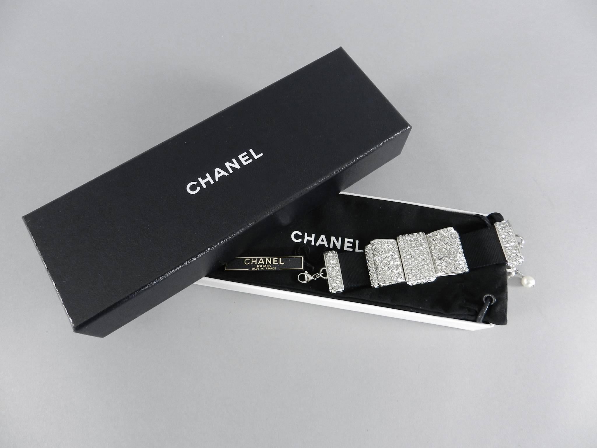 Chanel 13B rhinestone jewelled Bow Bracelet.  Silvertone metal with rhinestones on thick black grosgrain ribbon band. Extender chain is finished with a jewelled CC charm and faux pearl drop. Original retail price $2600+. Includes duster and box. To