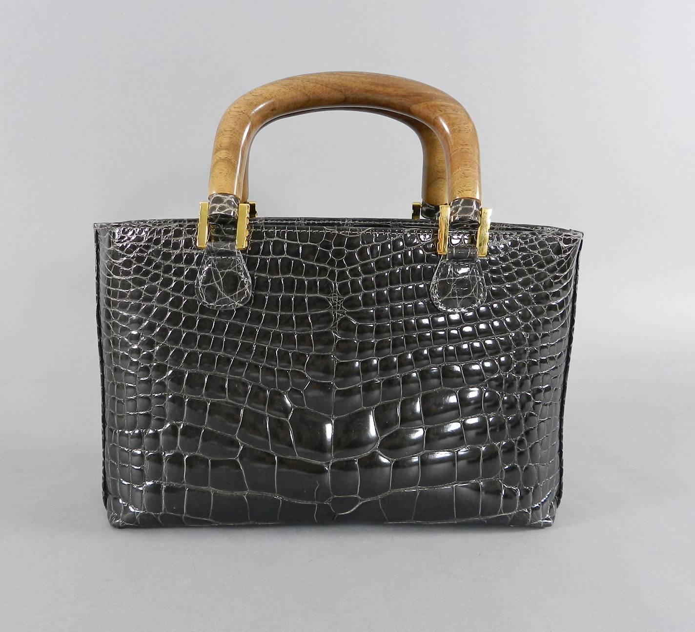 Lana Marks crocodile bag with wood handles, removable shoulder strap, and goldtone metal hardware.  Interior is lined with gray colored material. Color of bag is a dark gray with brownish tone - looks dark brown in some lighting. Measures 10 x 6.5 x